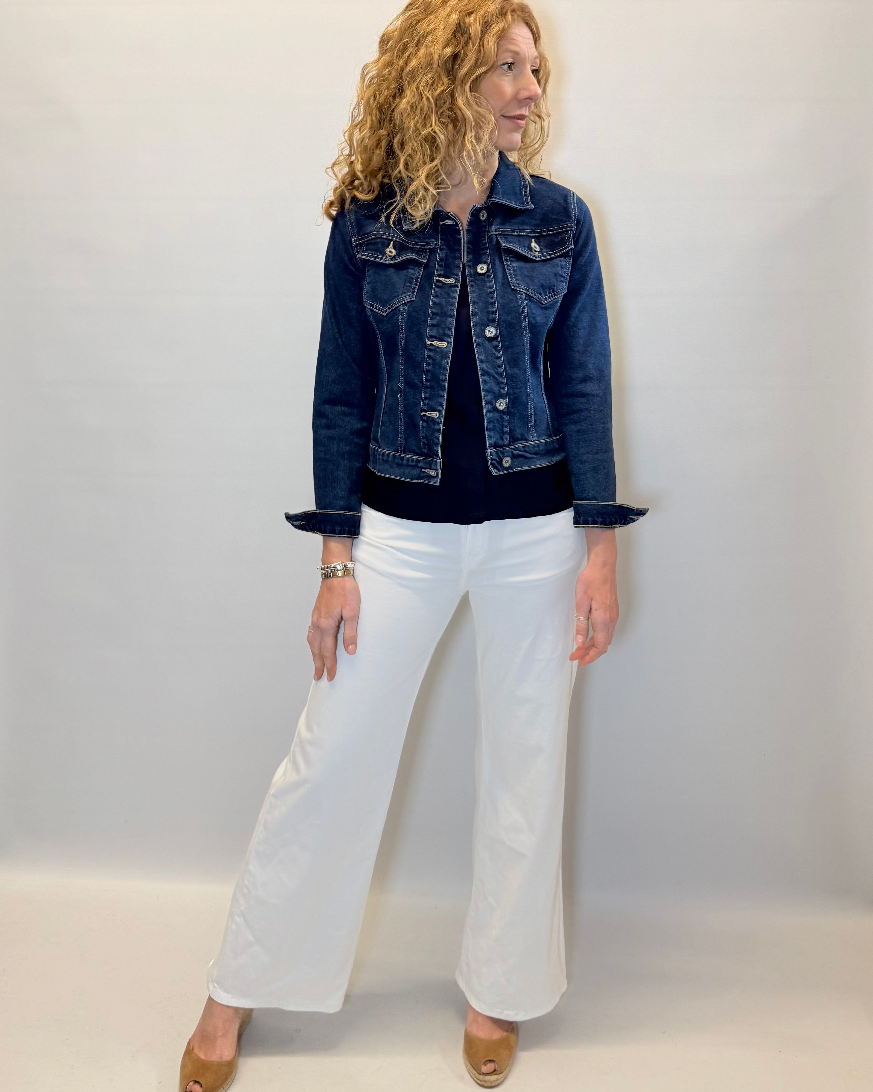 Woman wearing a denim jacket and white pants against a plain background