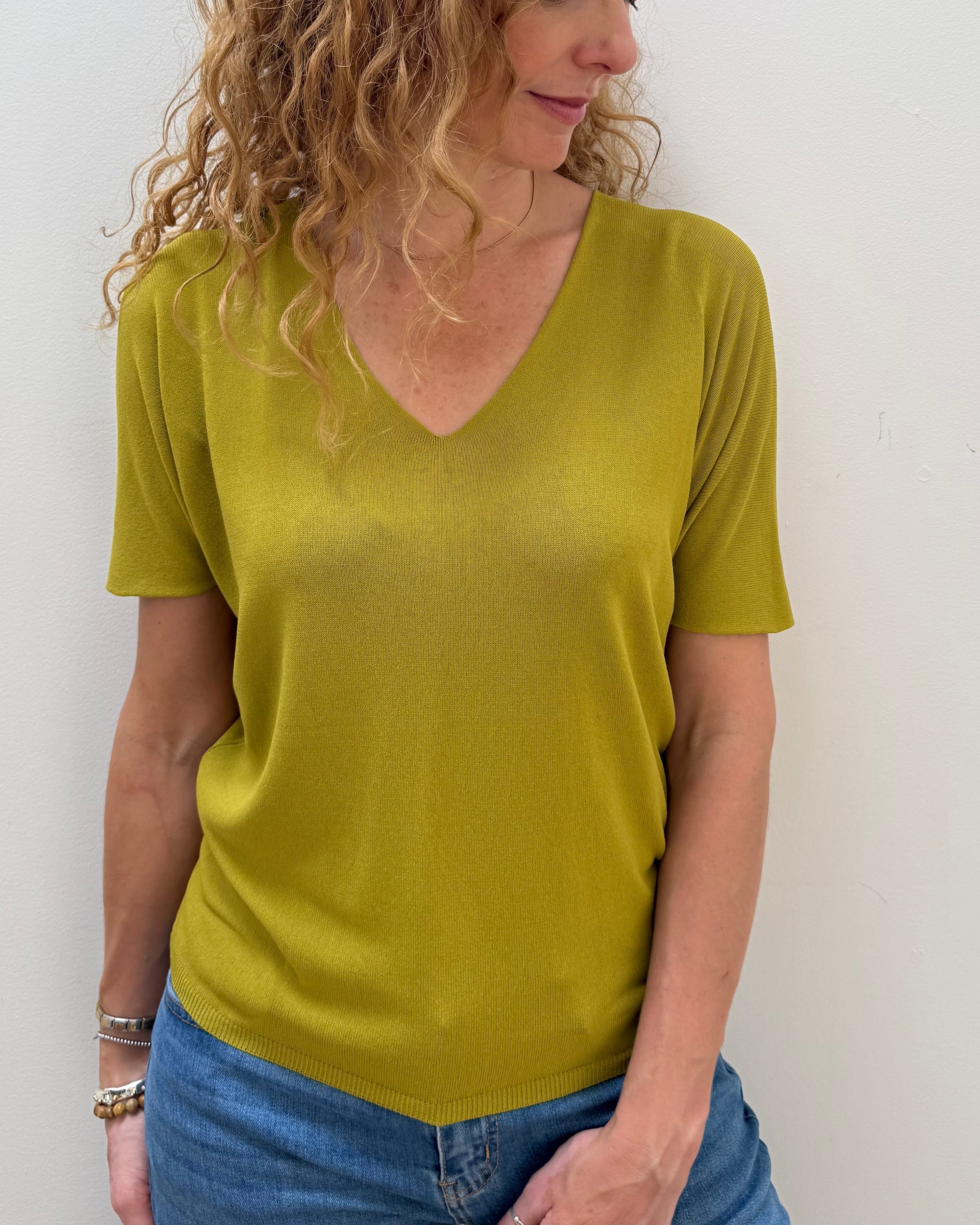 Woman wearing a green shirt and blue jeans against a white background