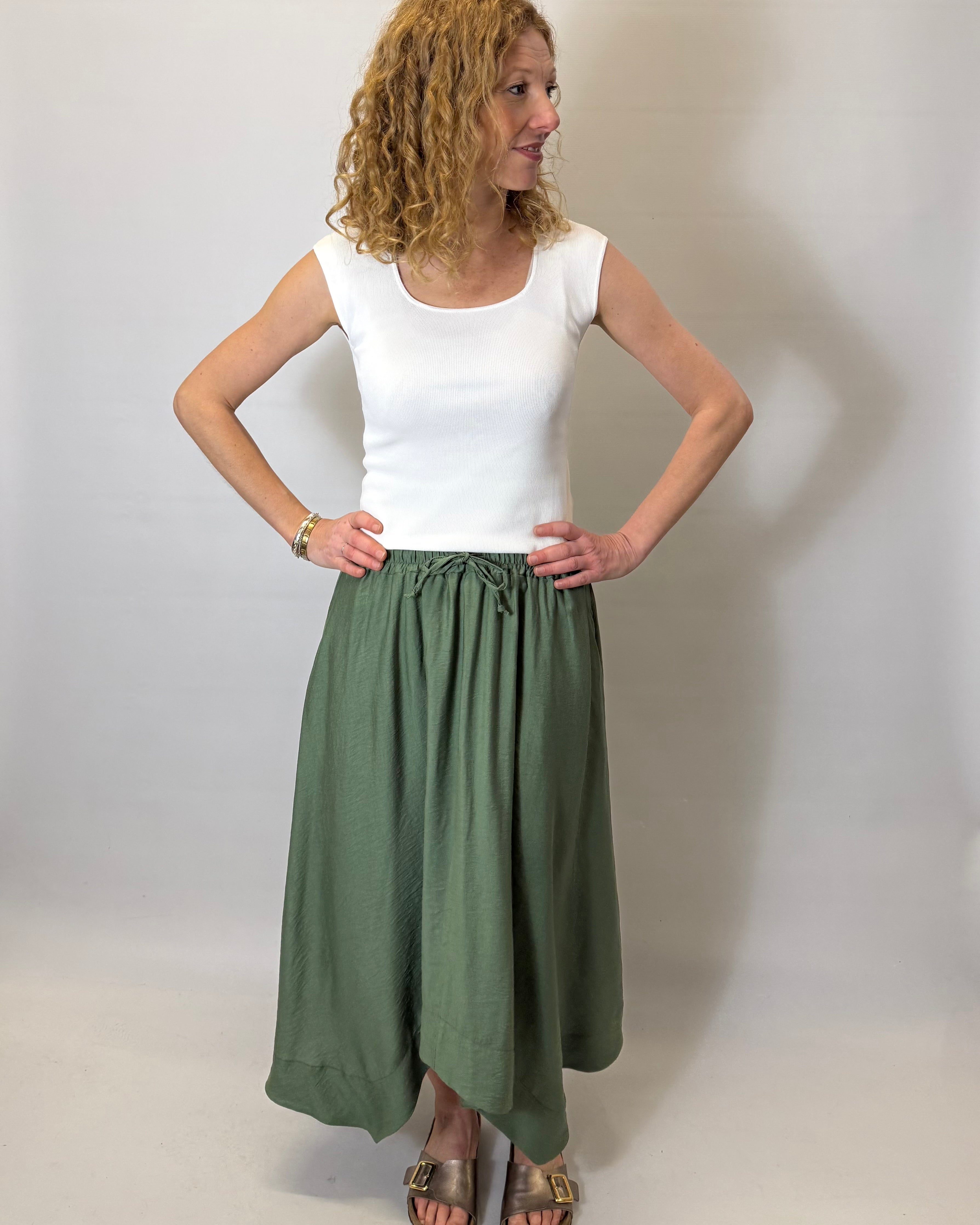 Woman wearing a white top and green skirt against a plain background