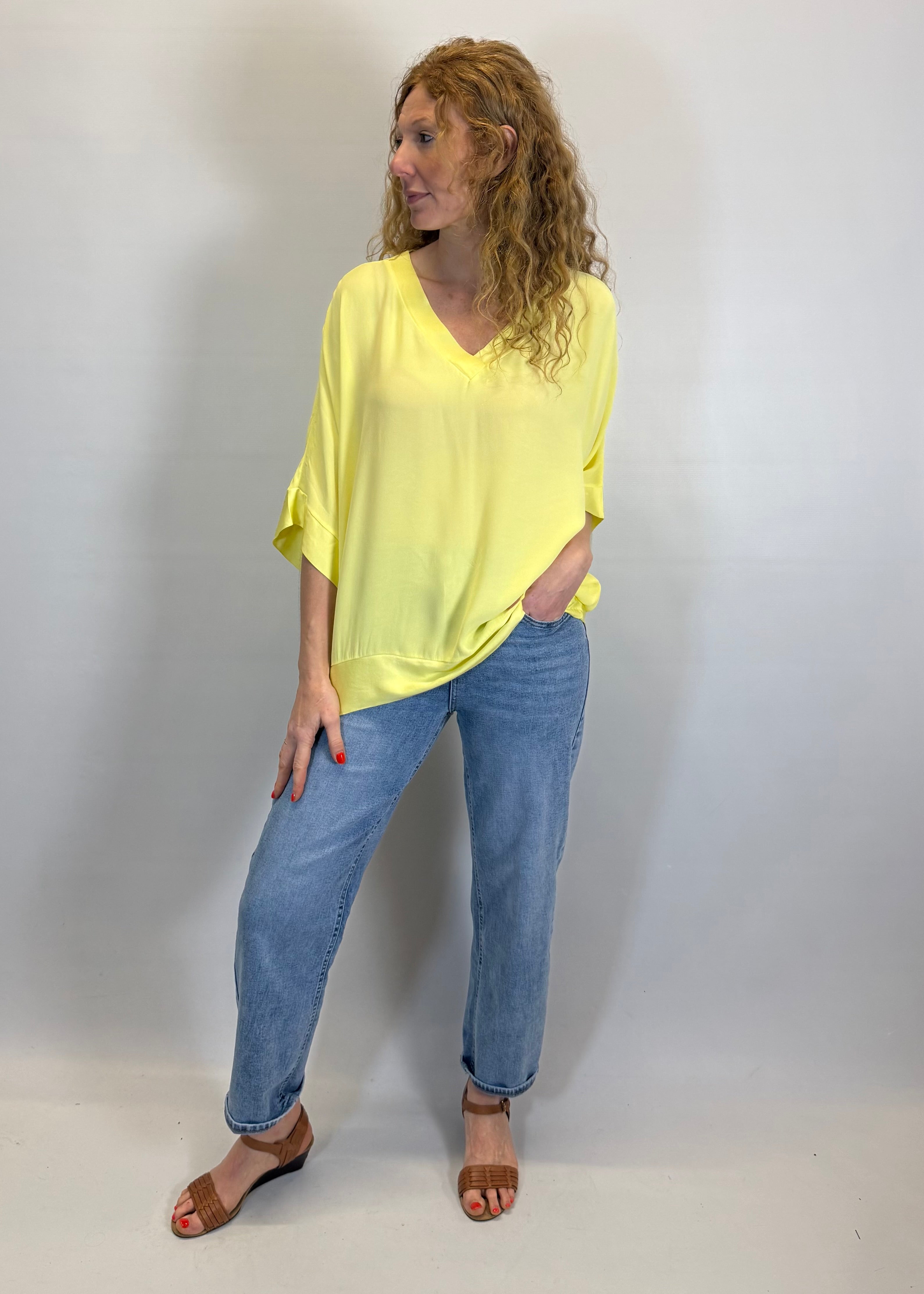 Woman wearing a yellow top and blue jeans against a white background
