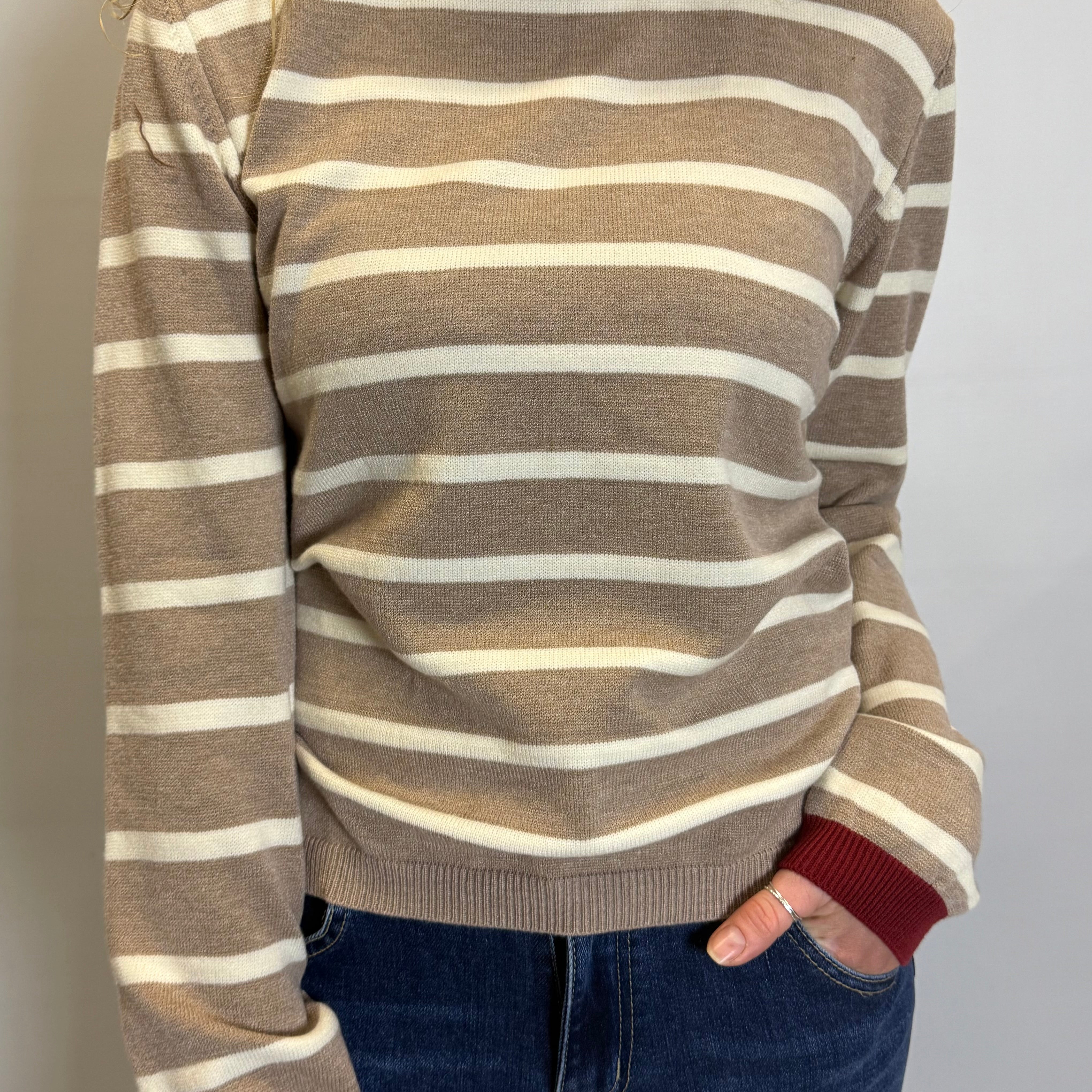 Person wearing a brown and beige striped sweater with red cuffs and collar against a plain background