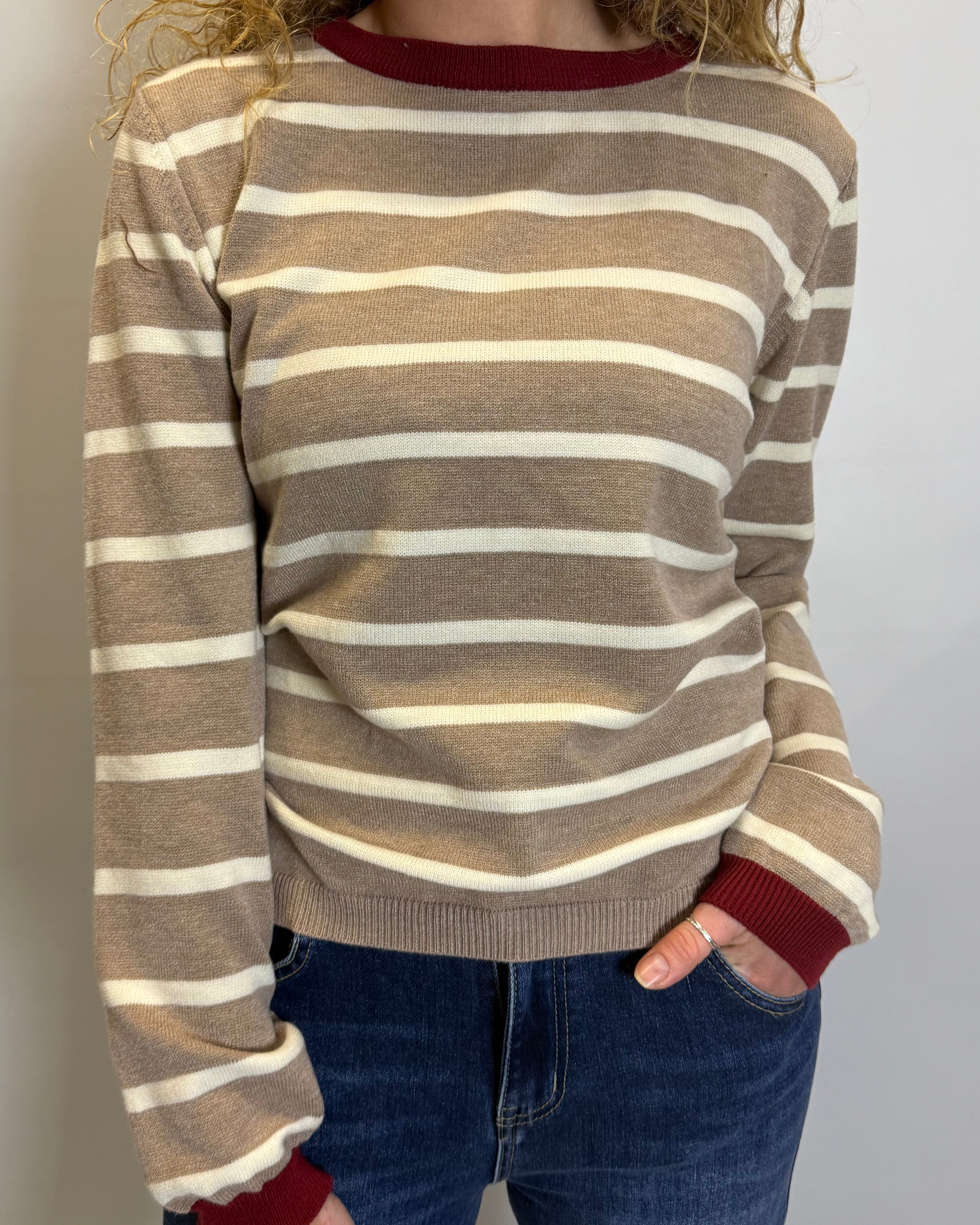 Person wearing a brown and beige striped sweater with red cuffs and collar against a plain background