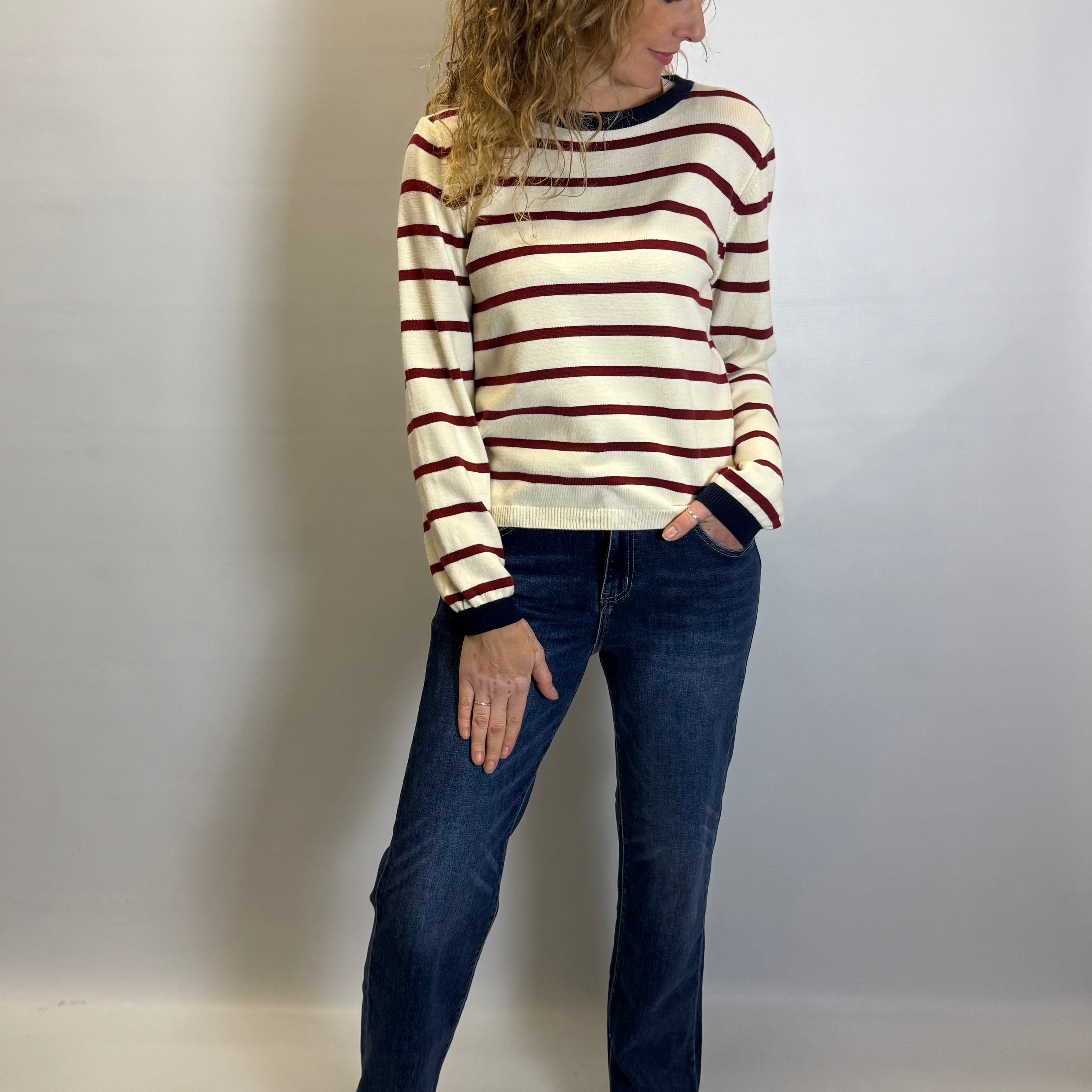 Woman wearing a striped sweater and jeans against a plain background