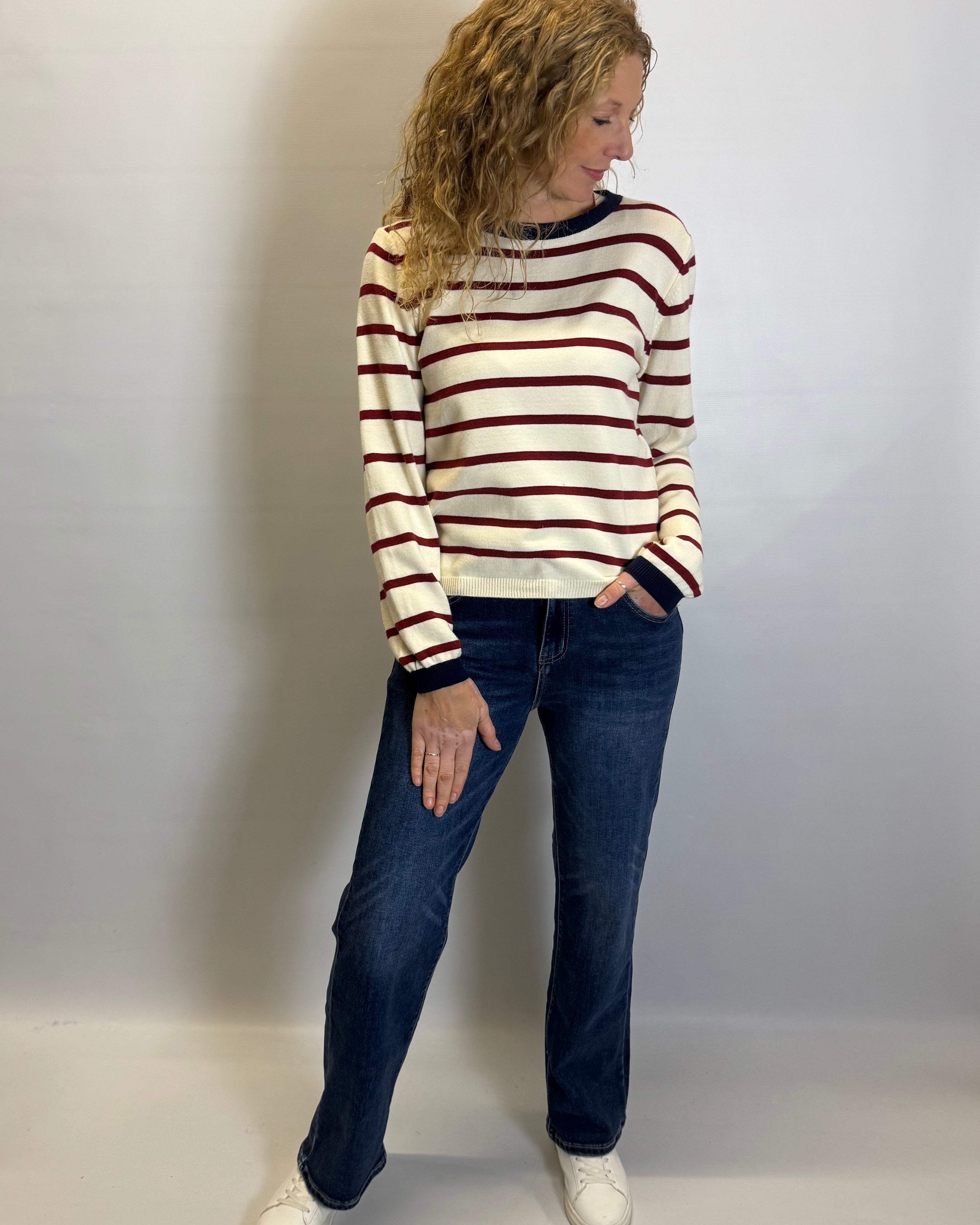Woman wearing a striped sweater and jeans against a plain background