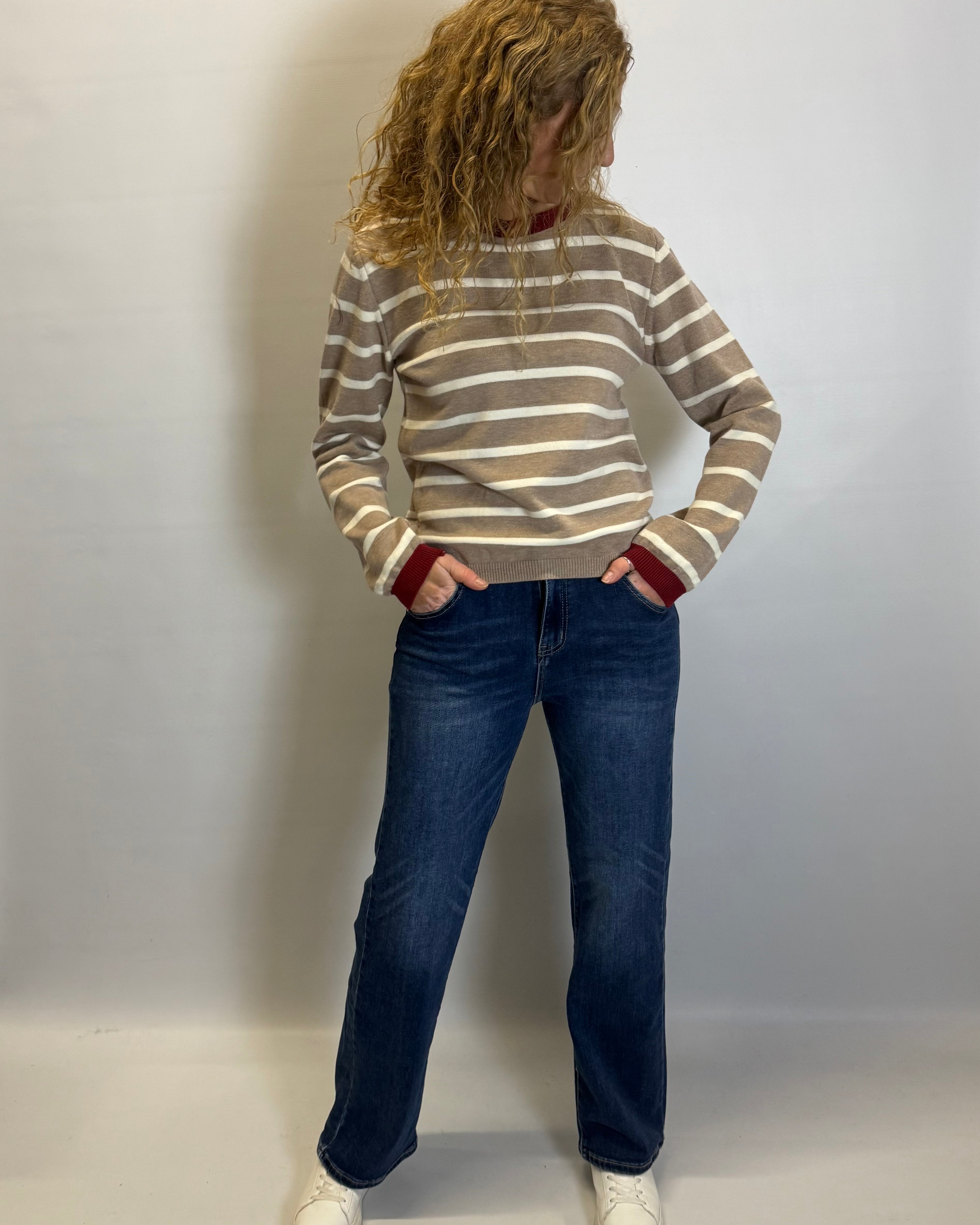 Person wearing a striped sweater and jeans against a plain background