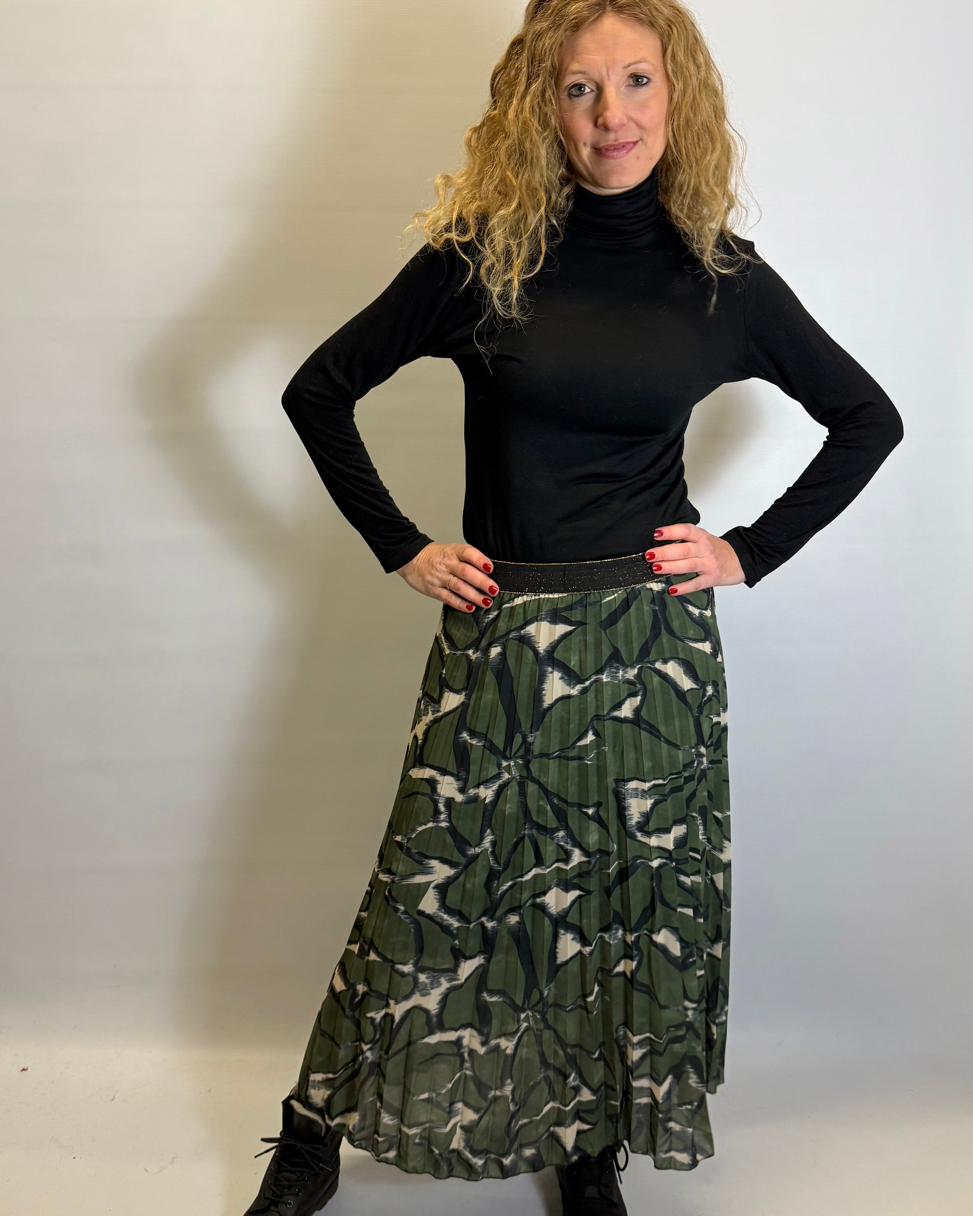 Woman wearing a black turtleneck and green patterned skirt against a white background