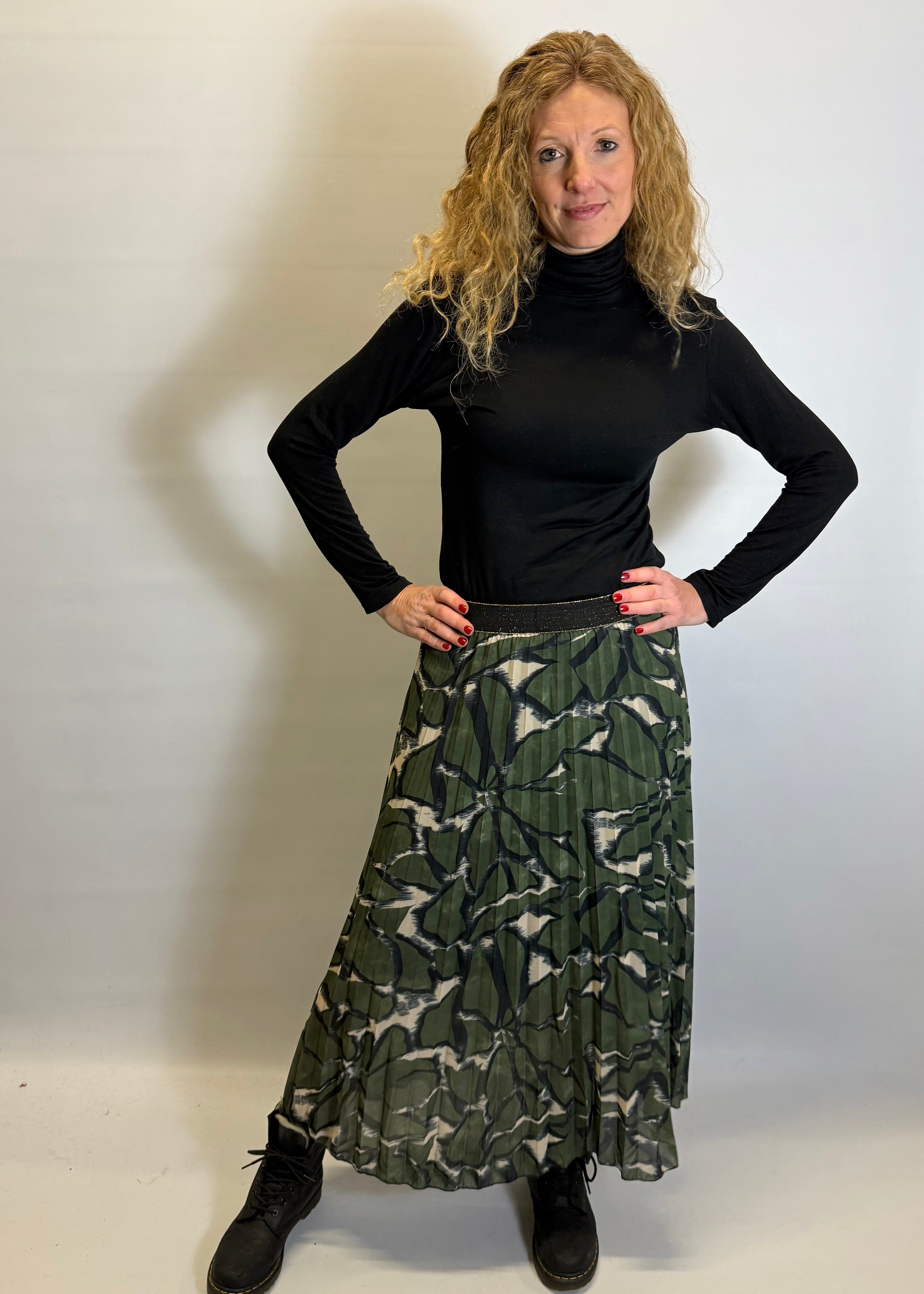 Woman wearing a black turtleneck and green patterned skirt against a white background