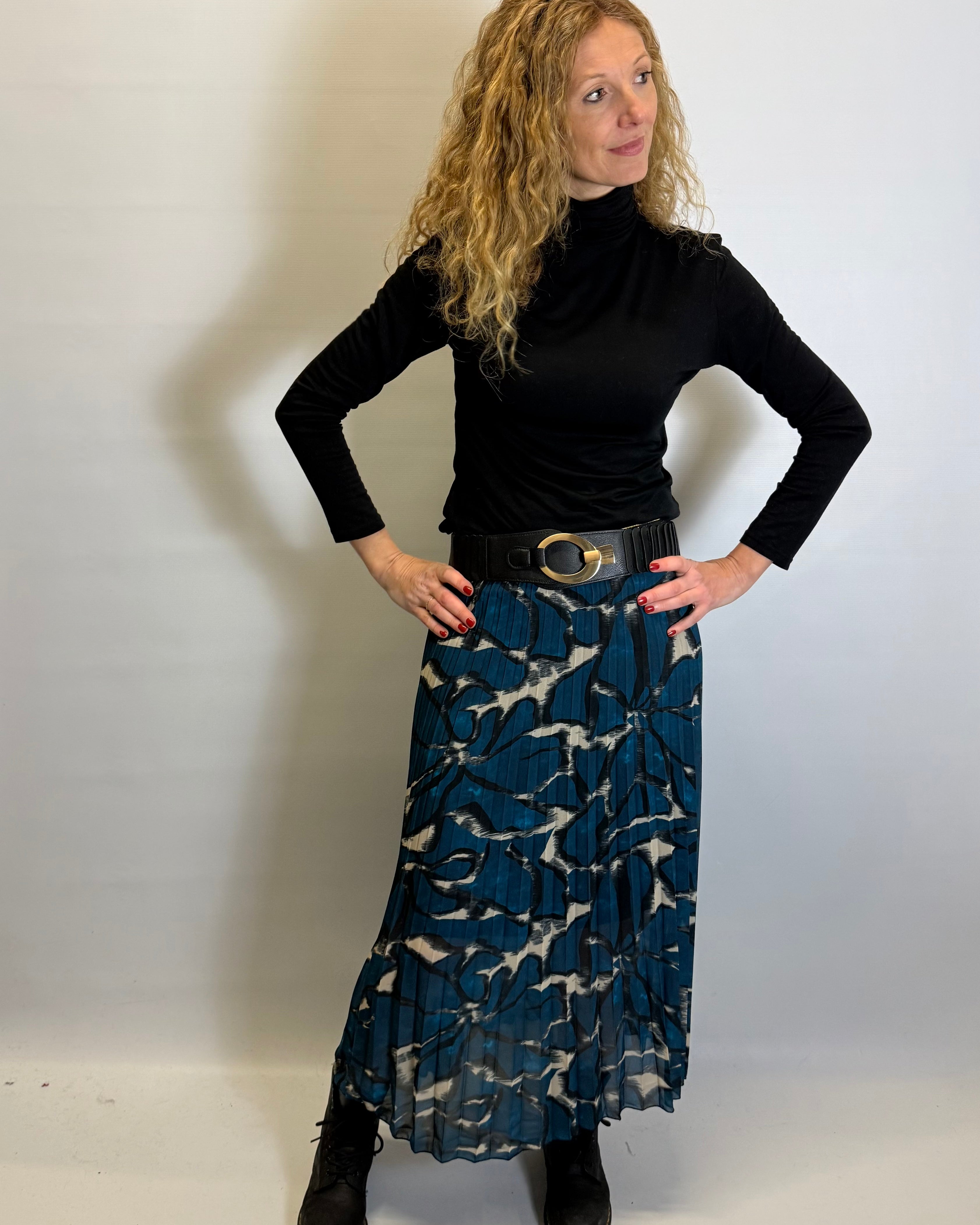 Woman wearing a black turtleneck and blue patterned skirt against a white background