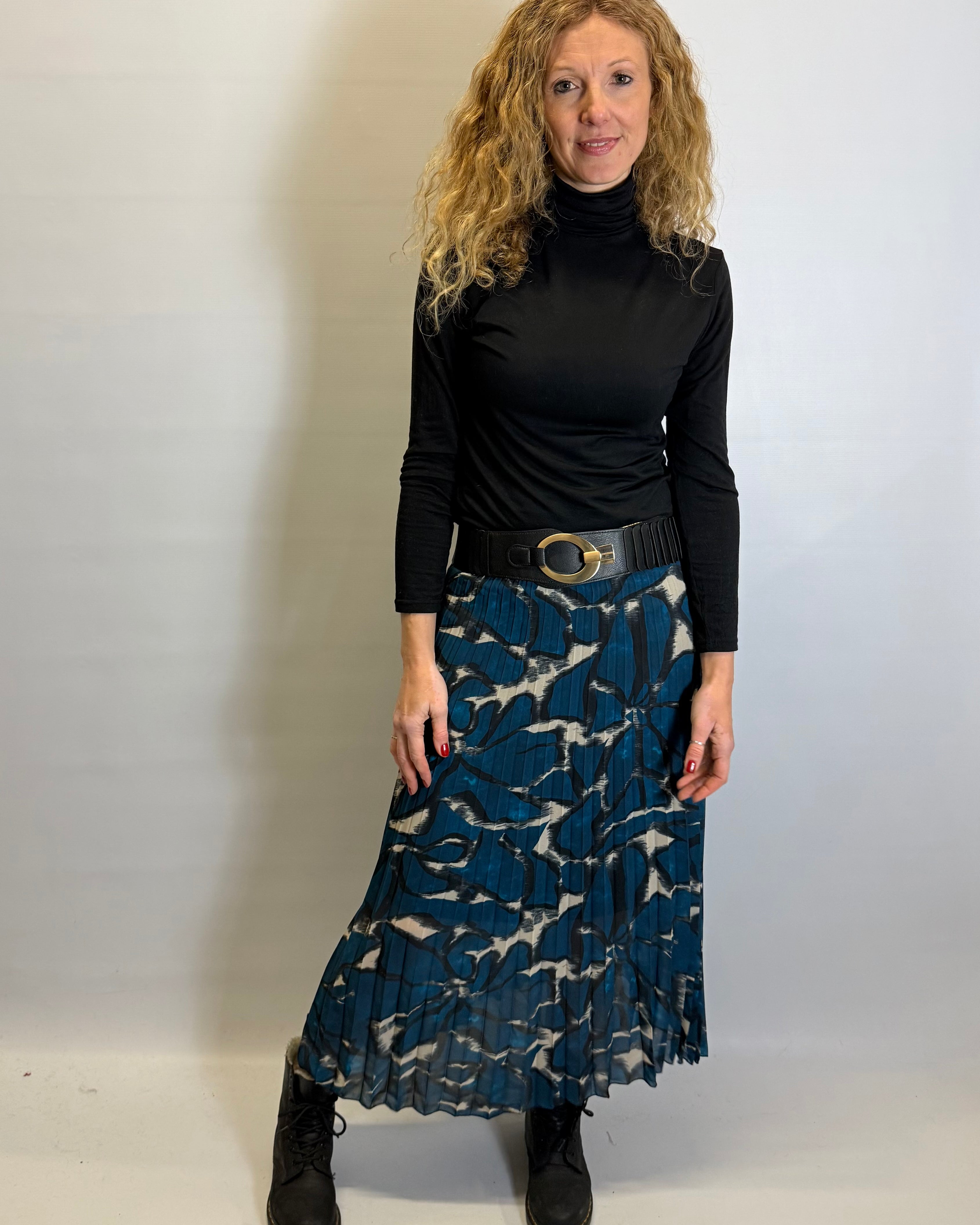 Woman wearing a black turtleneck and blue patterned skirt against a white background