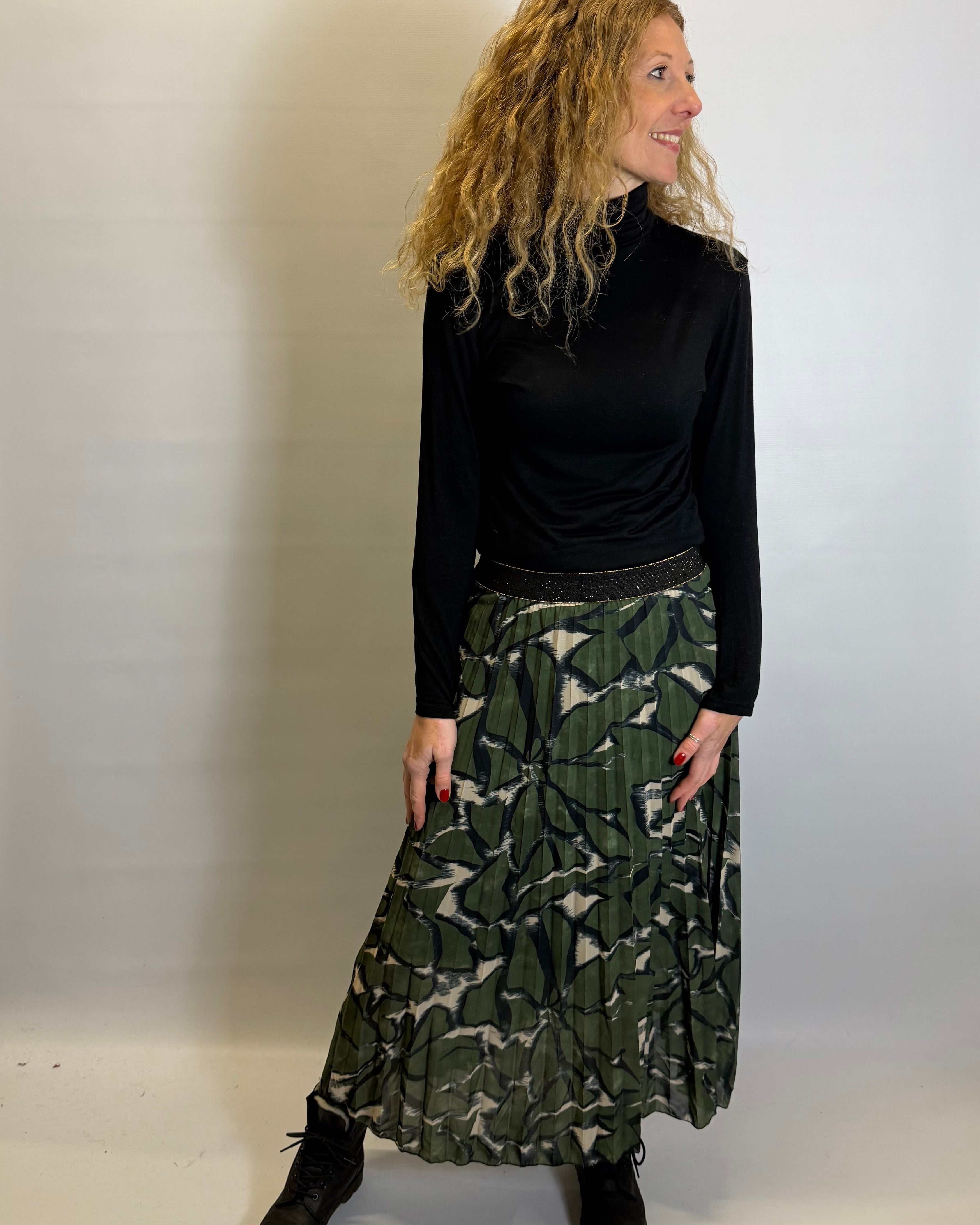 Woman wearing a black long-sleeve top and green patterned skirt against a white background