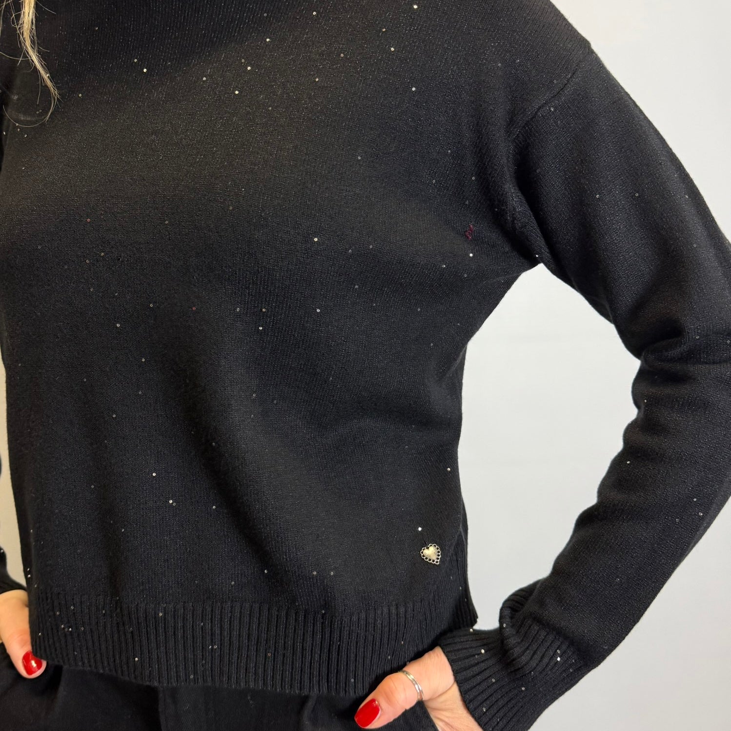 Person wearing a black sweater with sparkle stones on a plain background