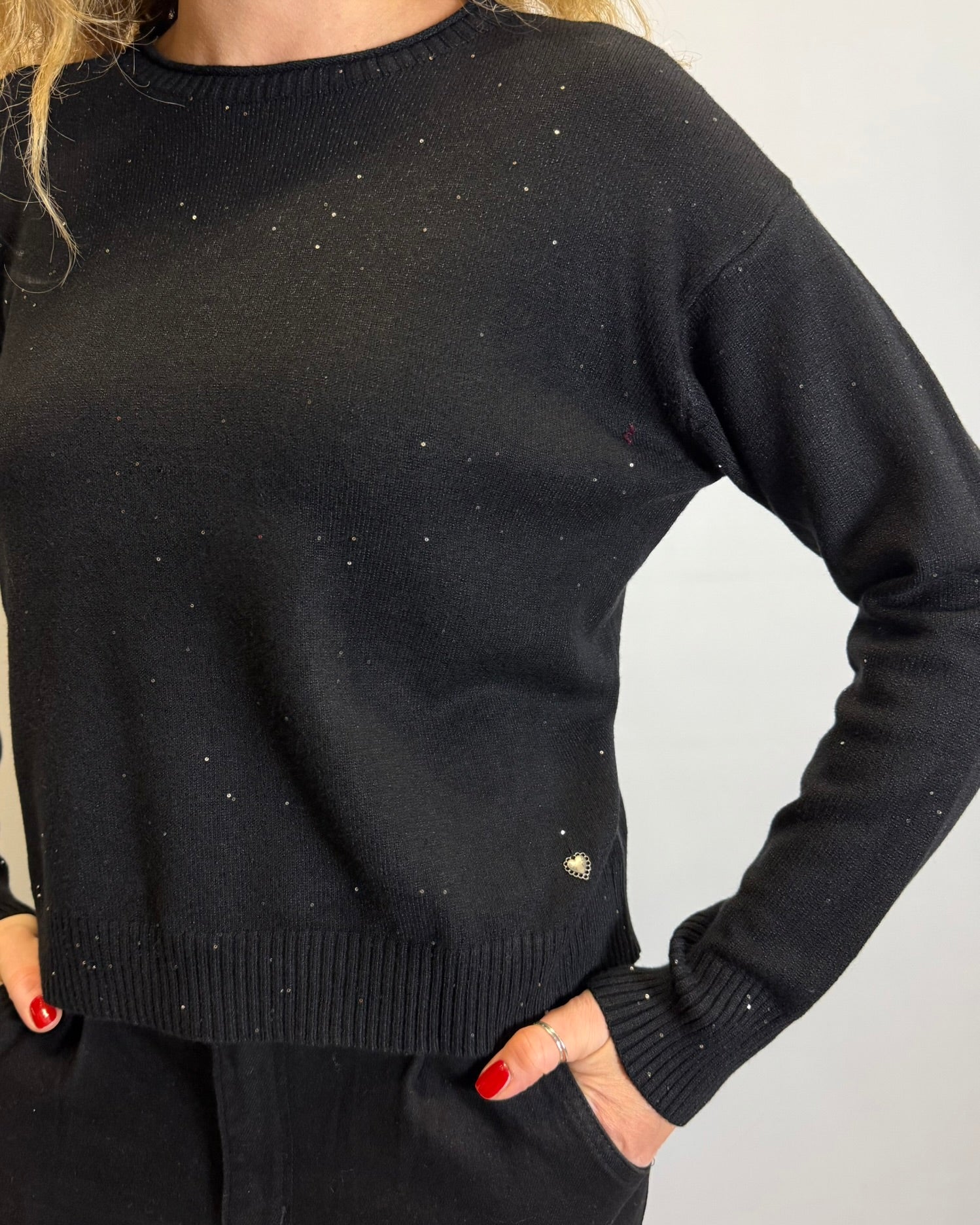 Person wearing a black sweater with sparkle stones on a plain background