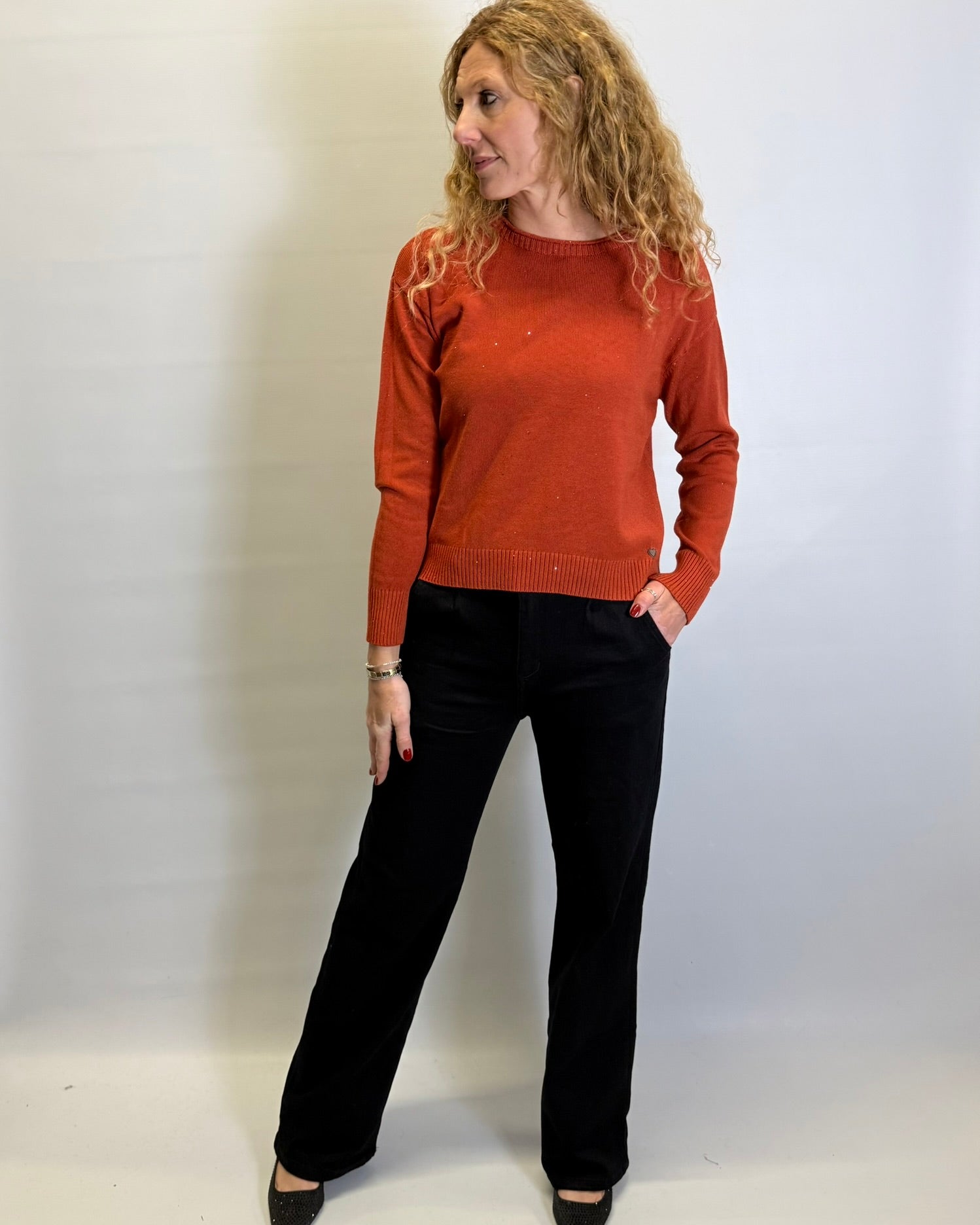 Woman wearing a rust-colored sweater and black pants against a white background