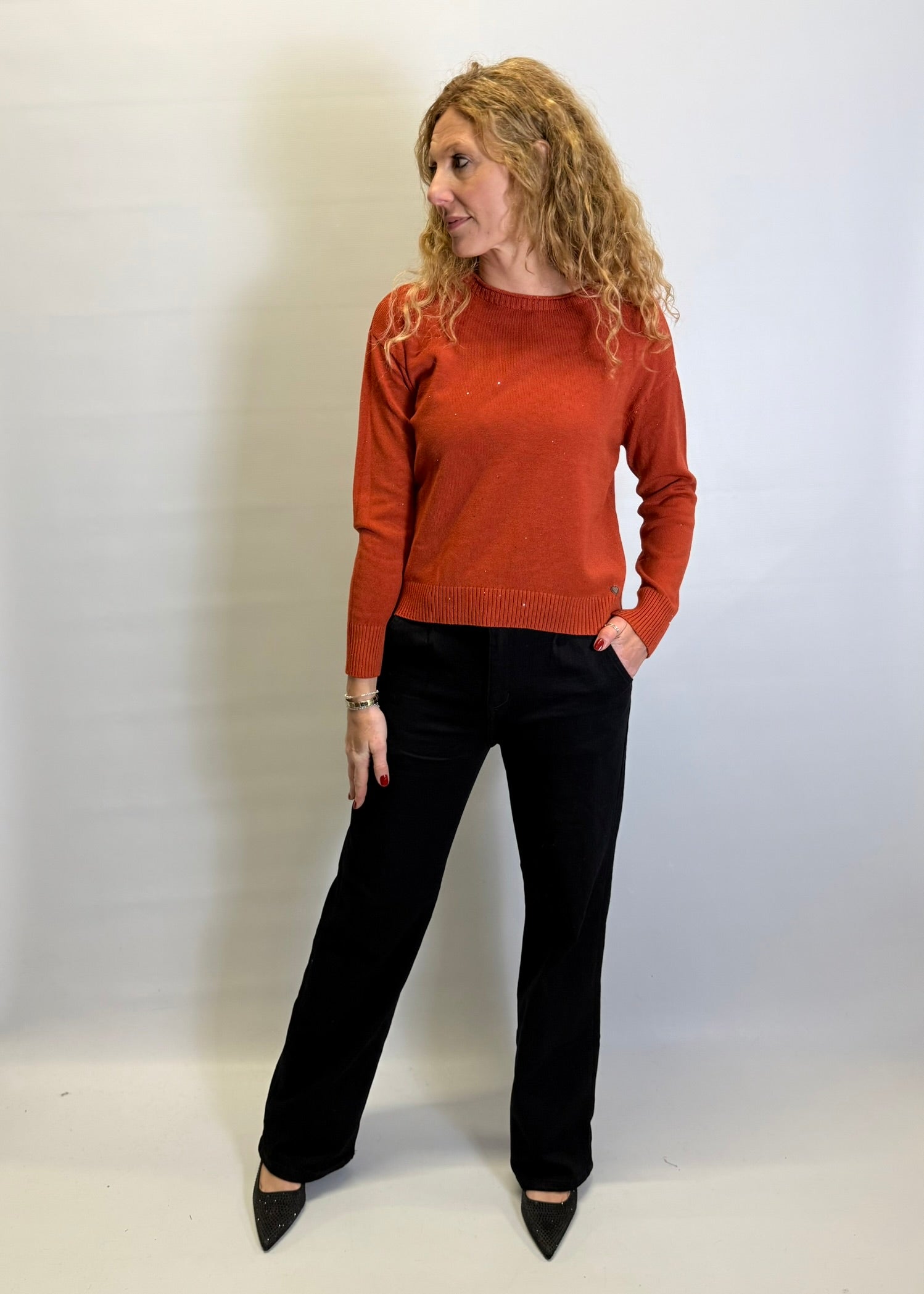 Woman wearing a rust-colored sweater and black pants against a white background