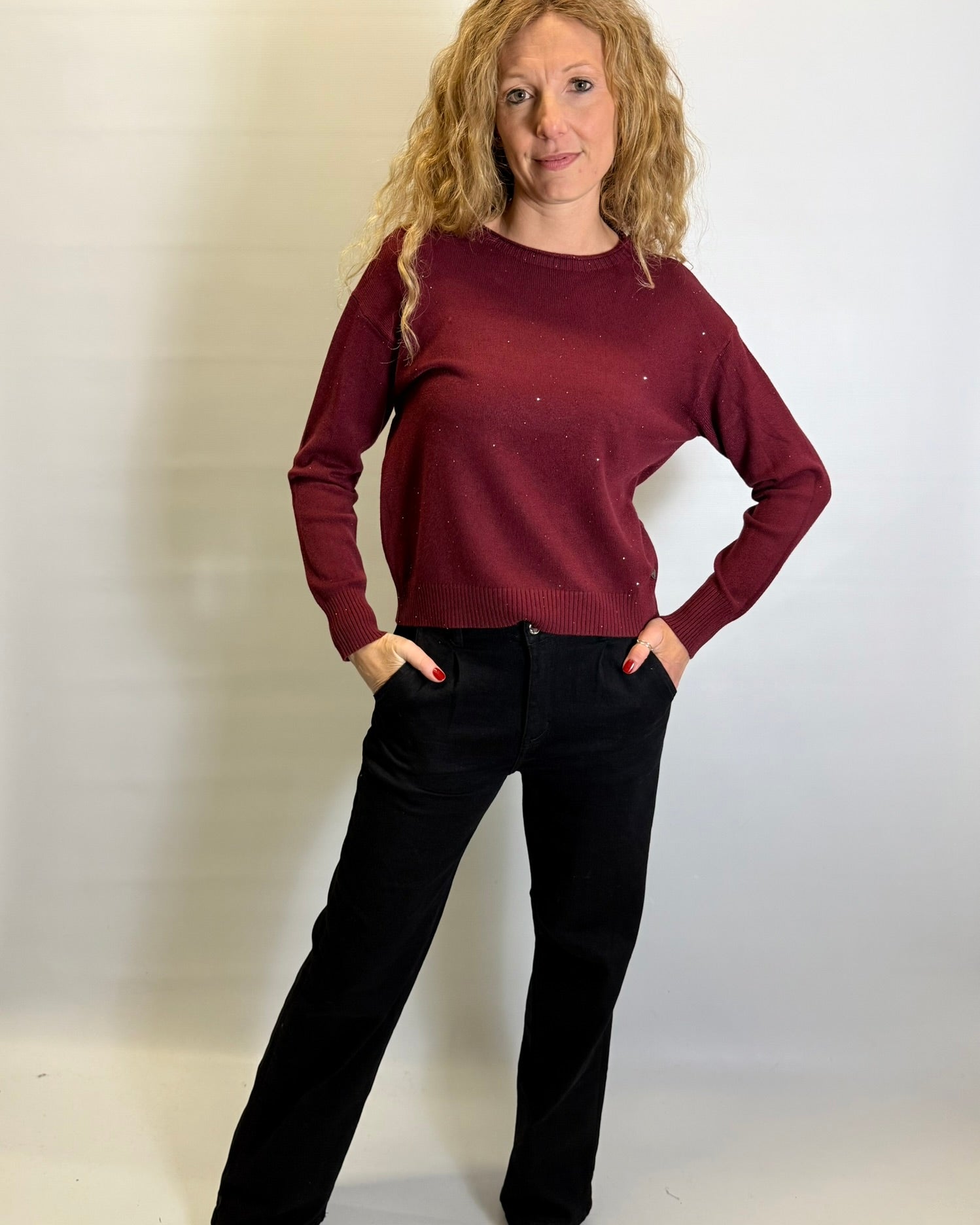 Woman wearing a burgundy sweater and black pants against a plain background