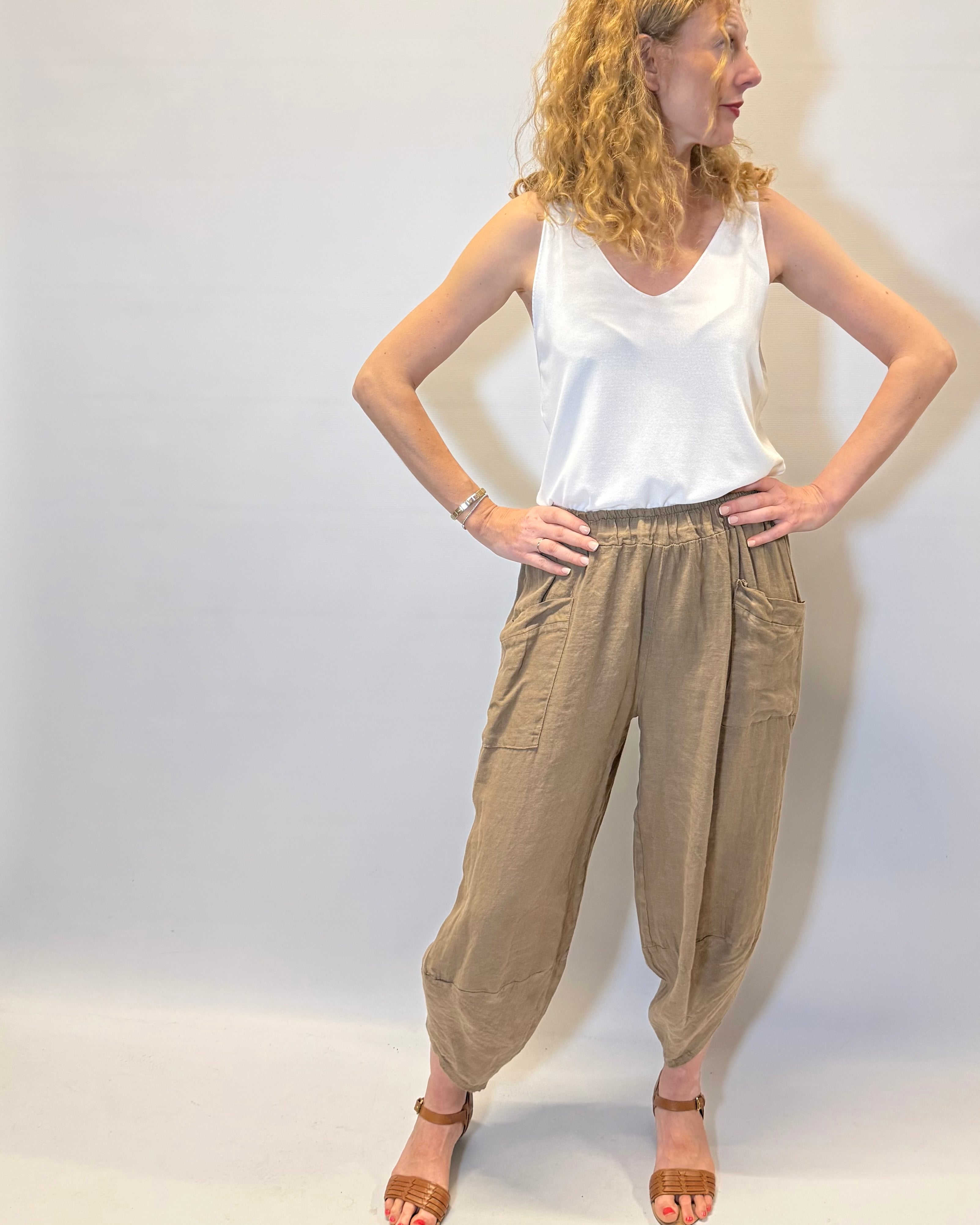 Woman wearing a white top and beige pants against a plain background