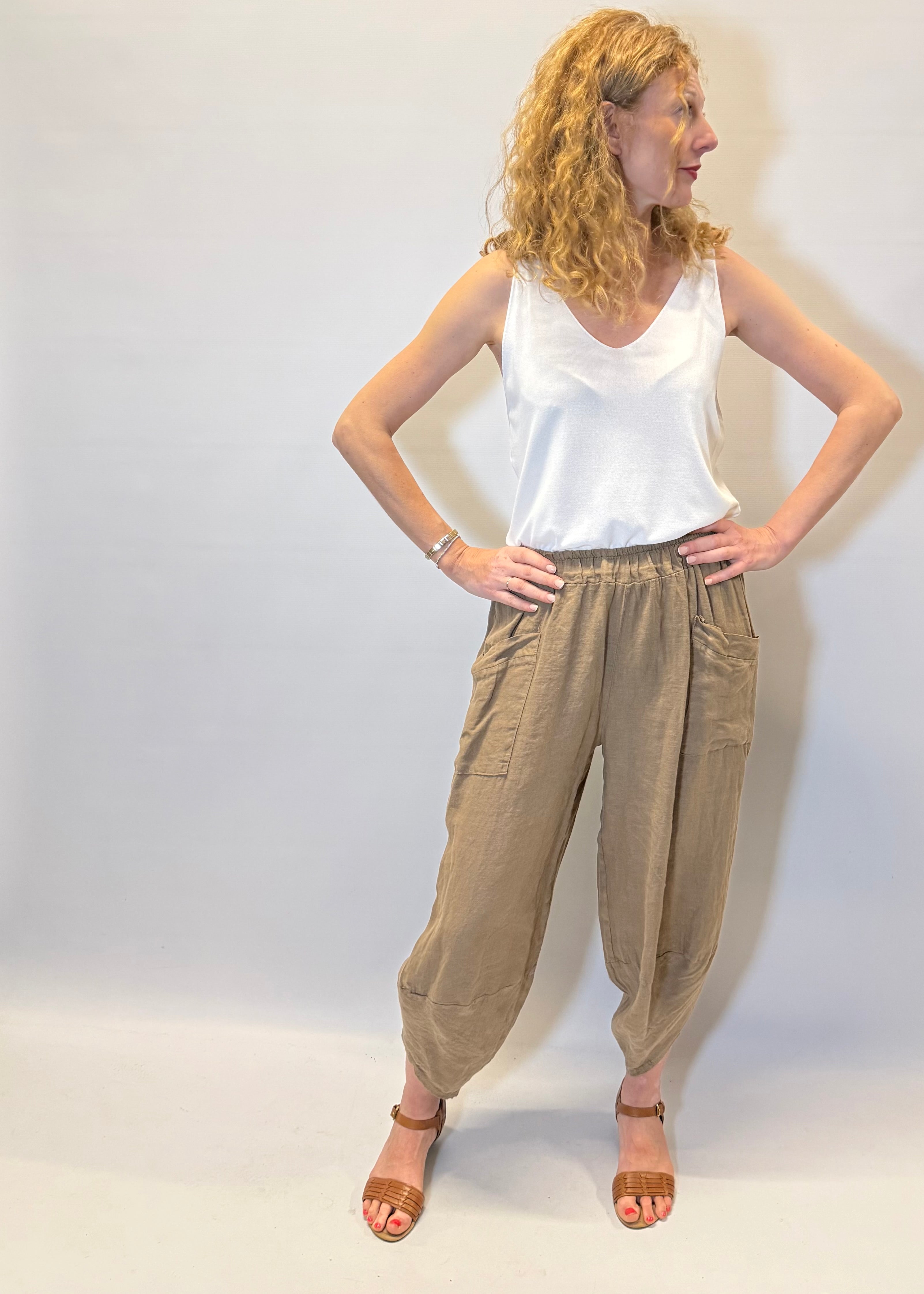 Woman wearing a white top and beige pants against a plain background