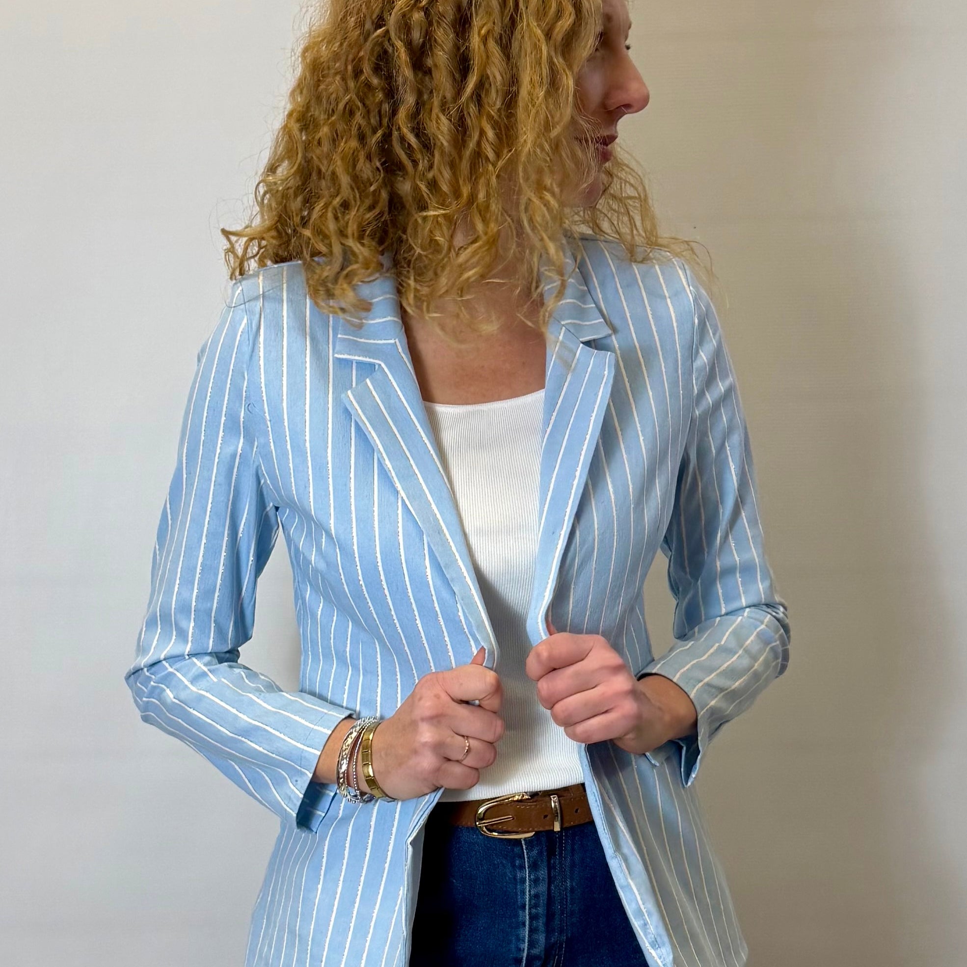 Woman wearing a light blue striped blazer over a white top and blue jeans against a plain background