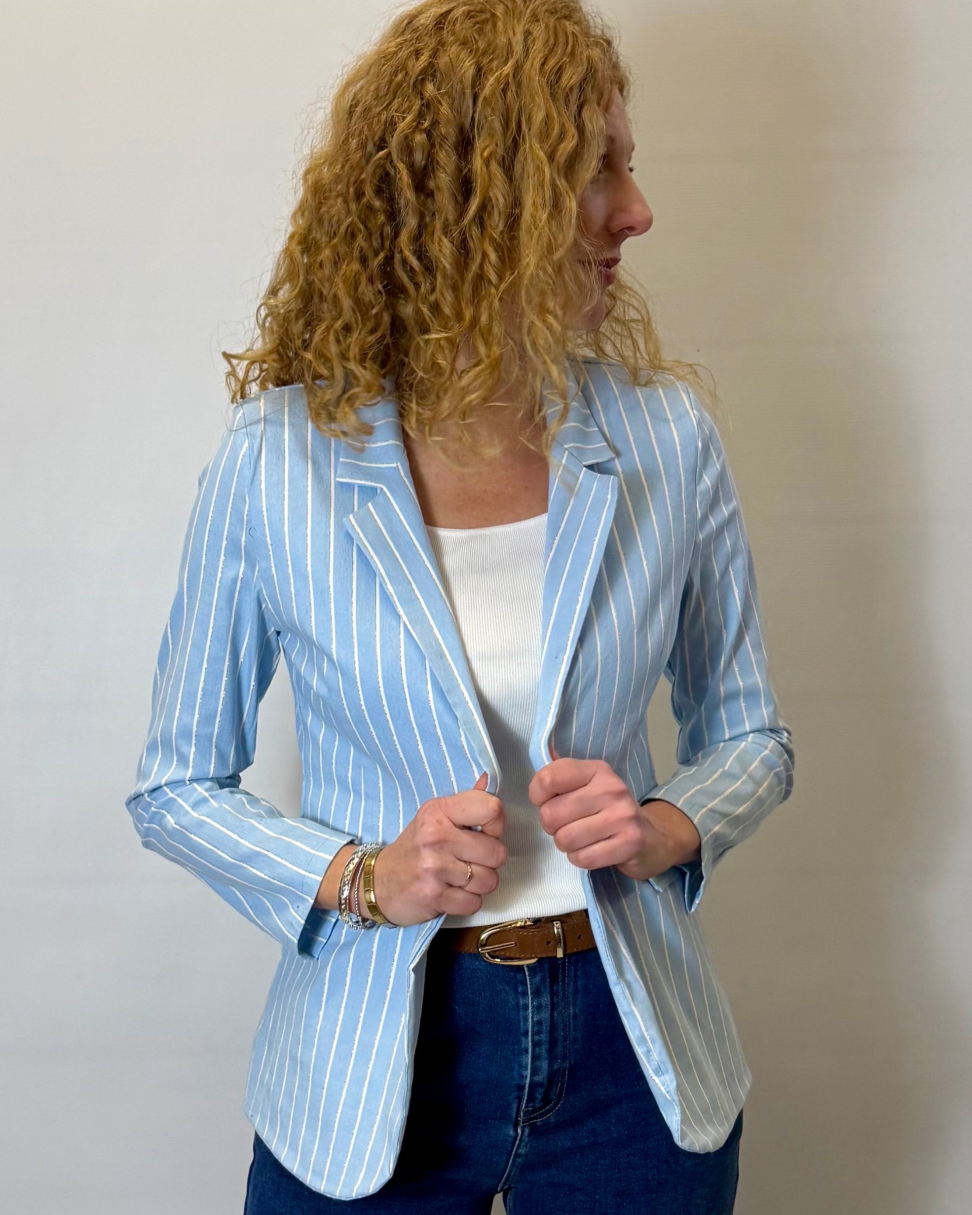 Woman wearing a light blue striped blazer over a white top and blue jeans against a plain background