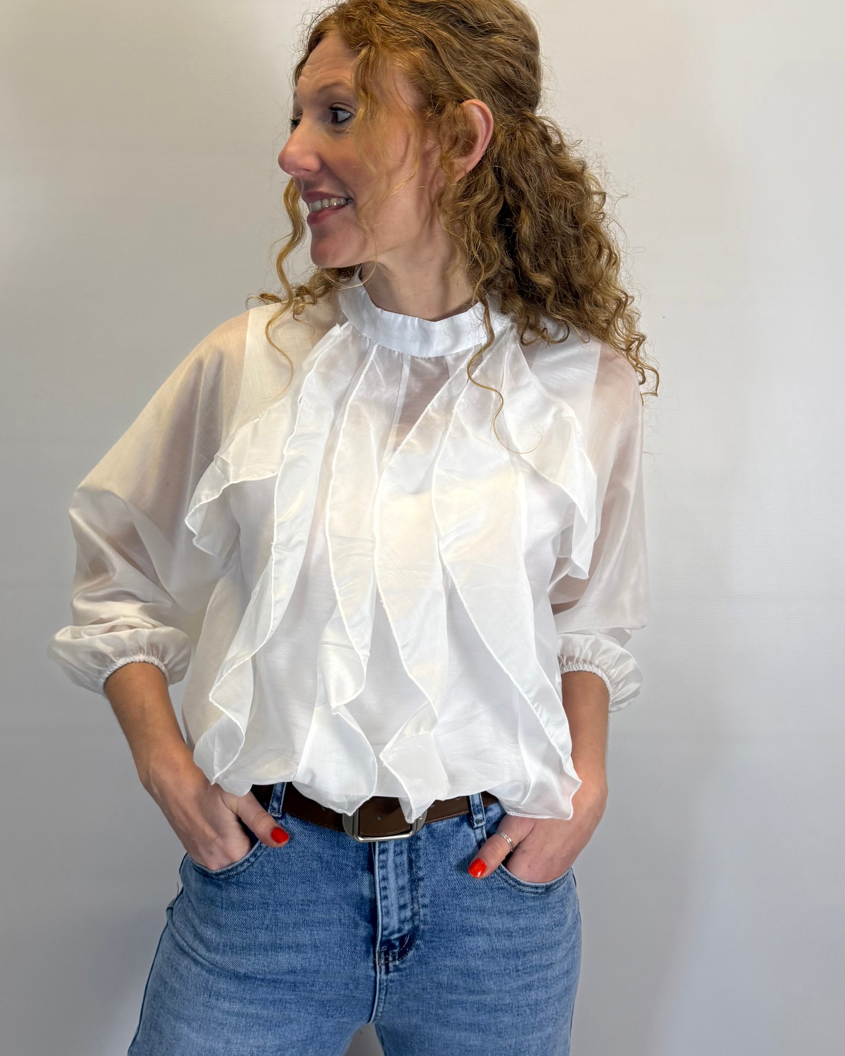 Woman wearing a white blouse with ruffled details and blue jeans against a plain background
