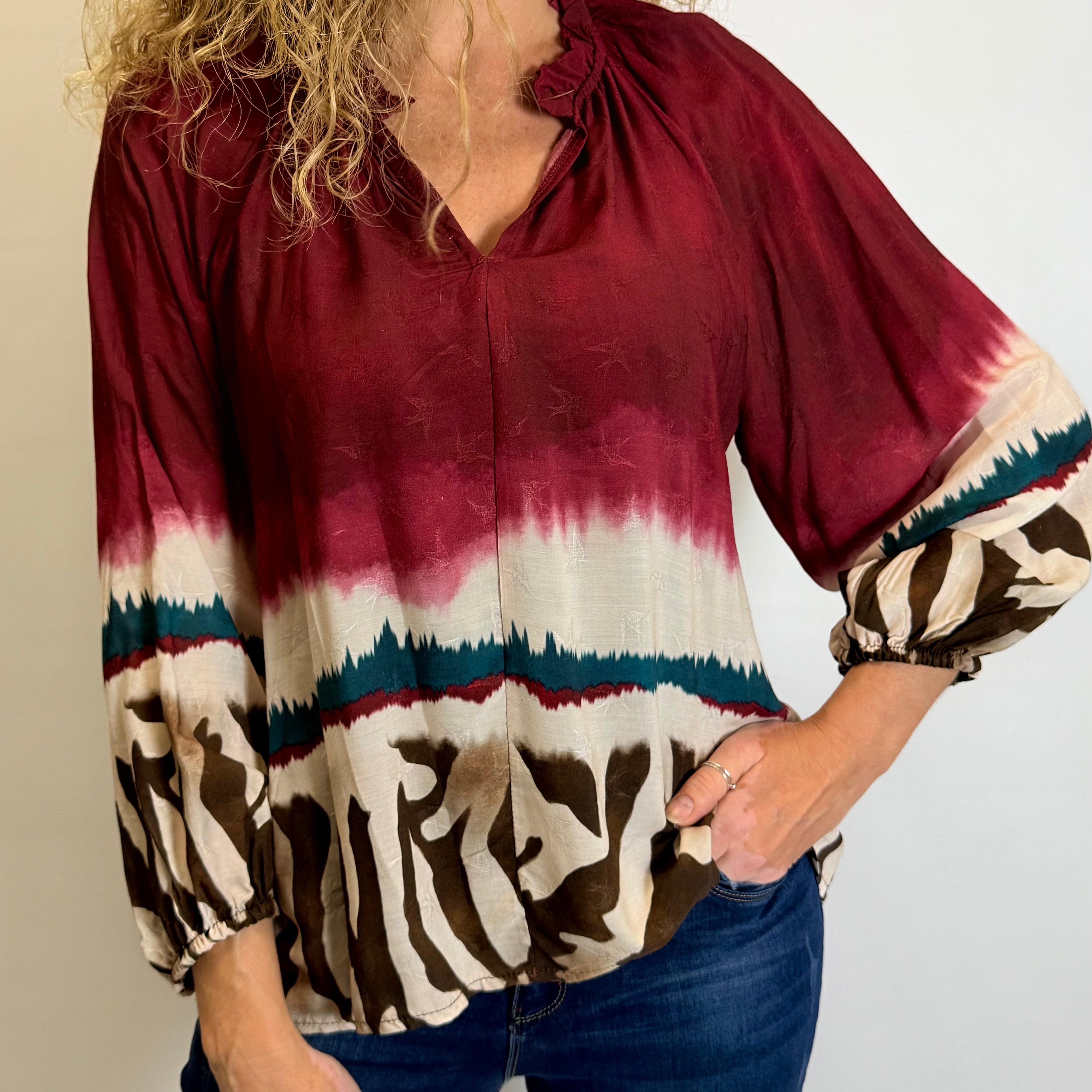 Woman wearing a burgundy tie-dye blouse with zebra print cuffs against a plain background