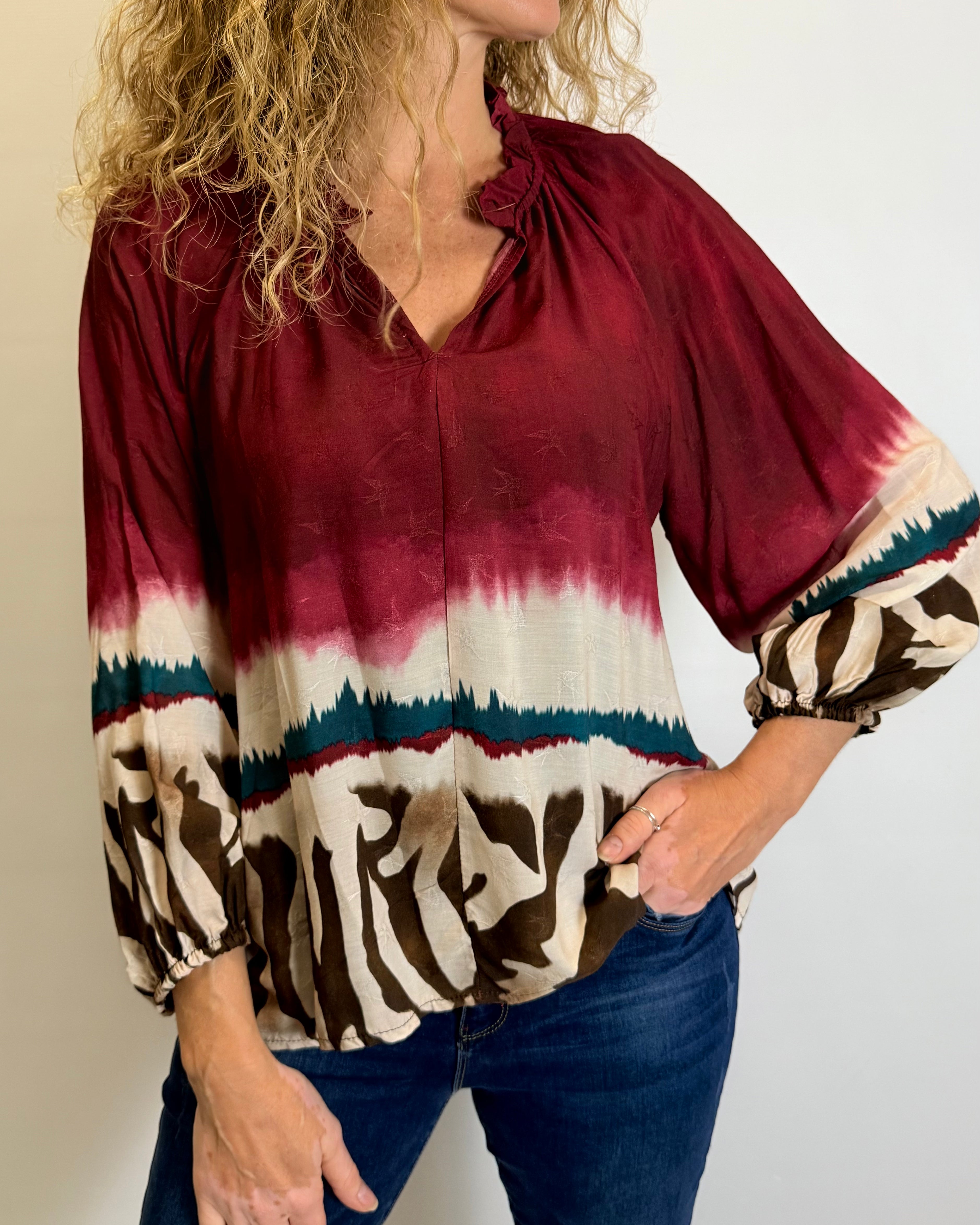 Woman wearing a burgundy tie-dye blouse with zebra print cuffs against a plain background