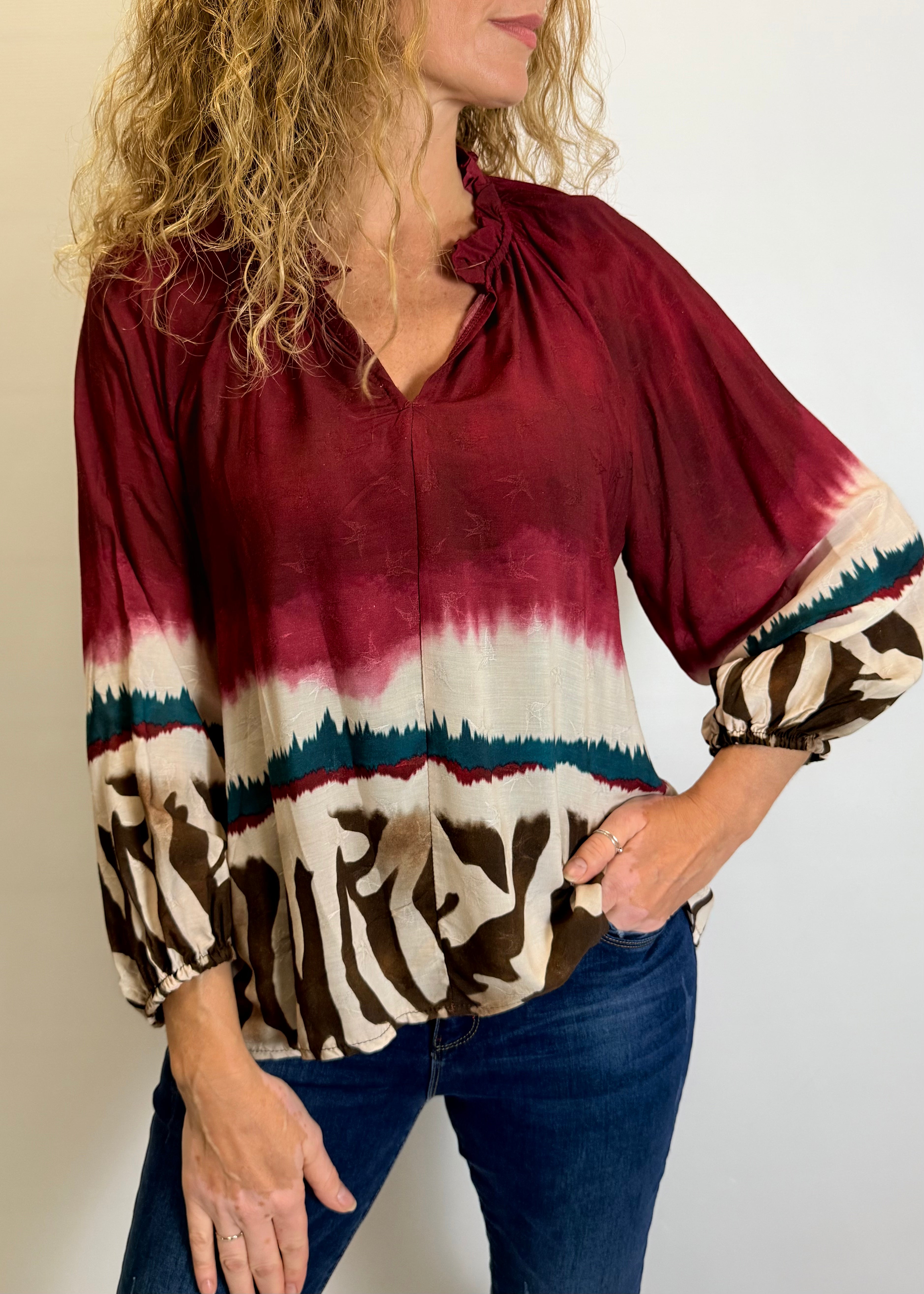 Woman wearing a burgundy tie-dye blouse with zebra print cuffs against a plain background