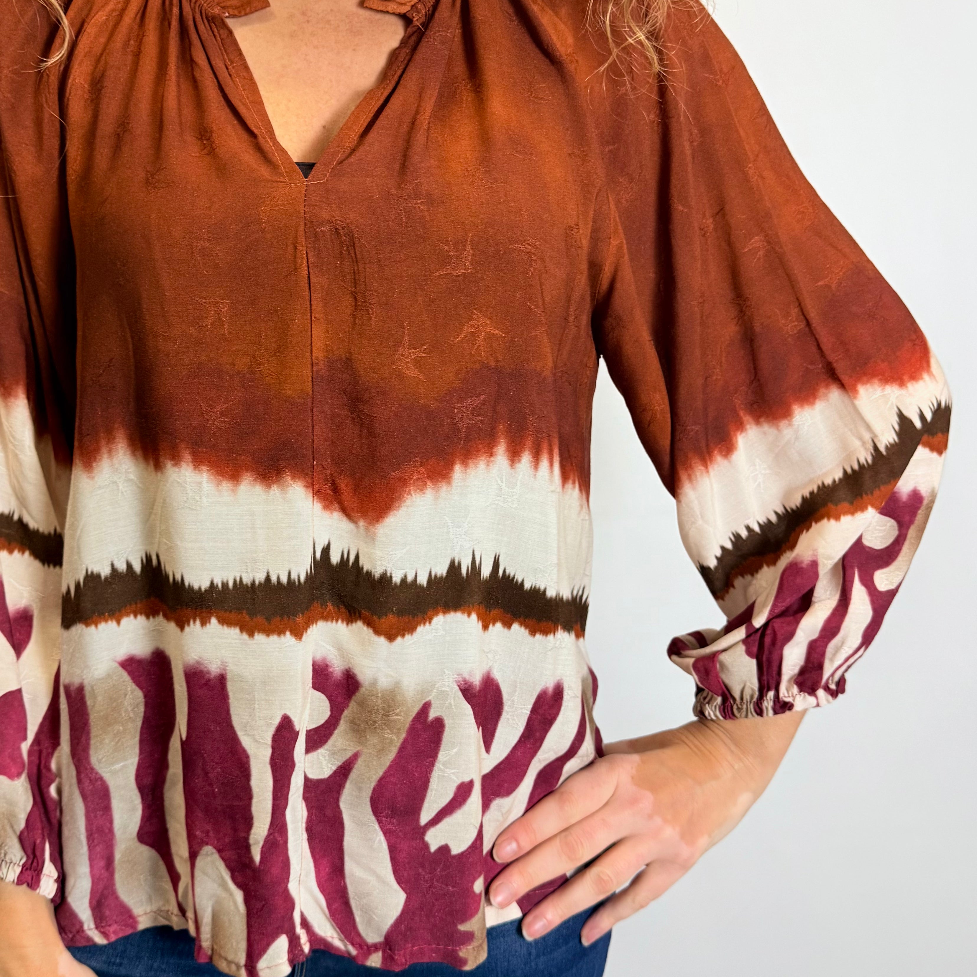 Person wearing a tie-dye blouse with rust, white, and maroon colors on a plain background