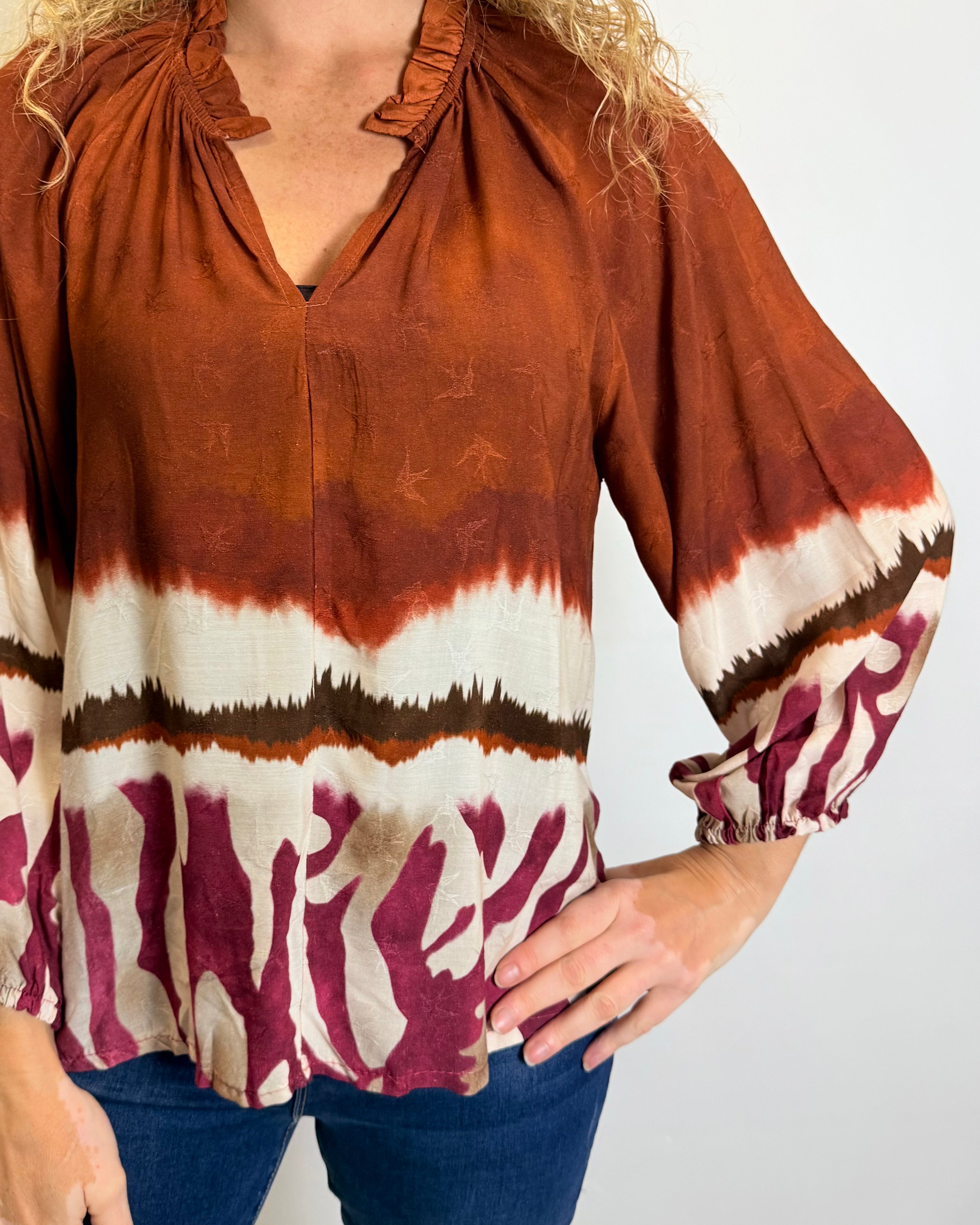 Person wearing a tie-dye blouse with rust, white, and maroon colors on a plain background