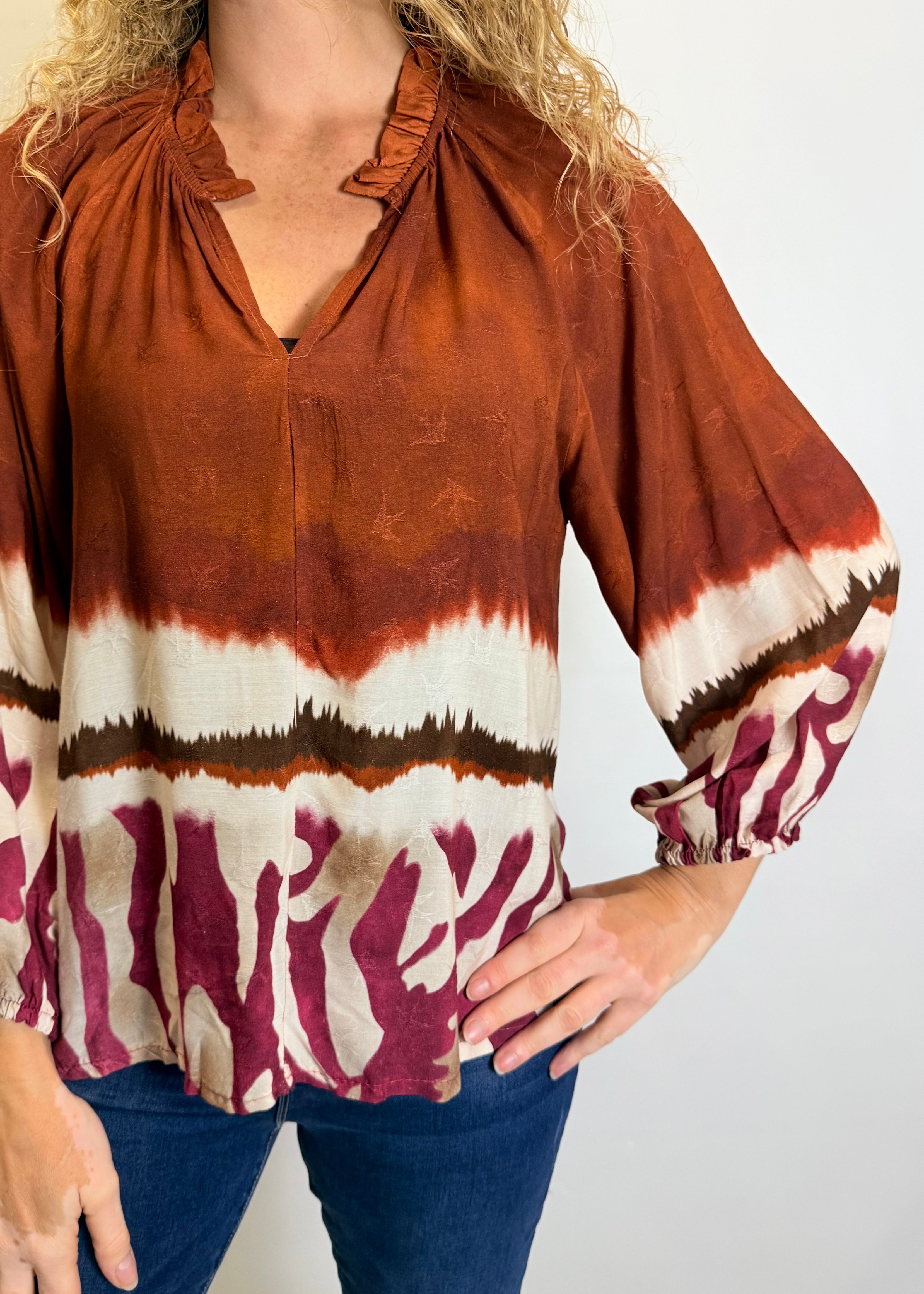 Person wearing a tie-dye blouse with rust, white, and maroon colors on a plain background