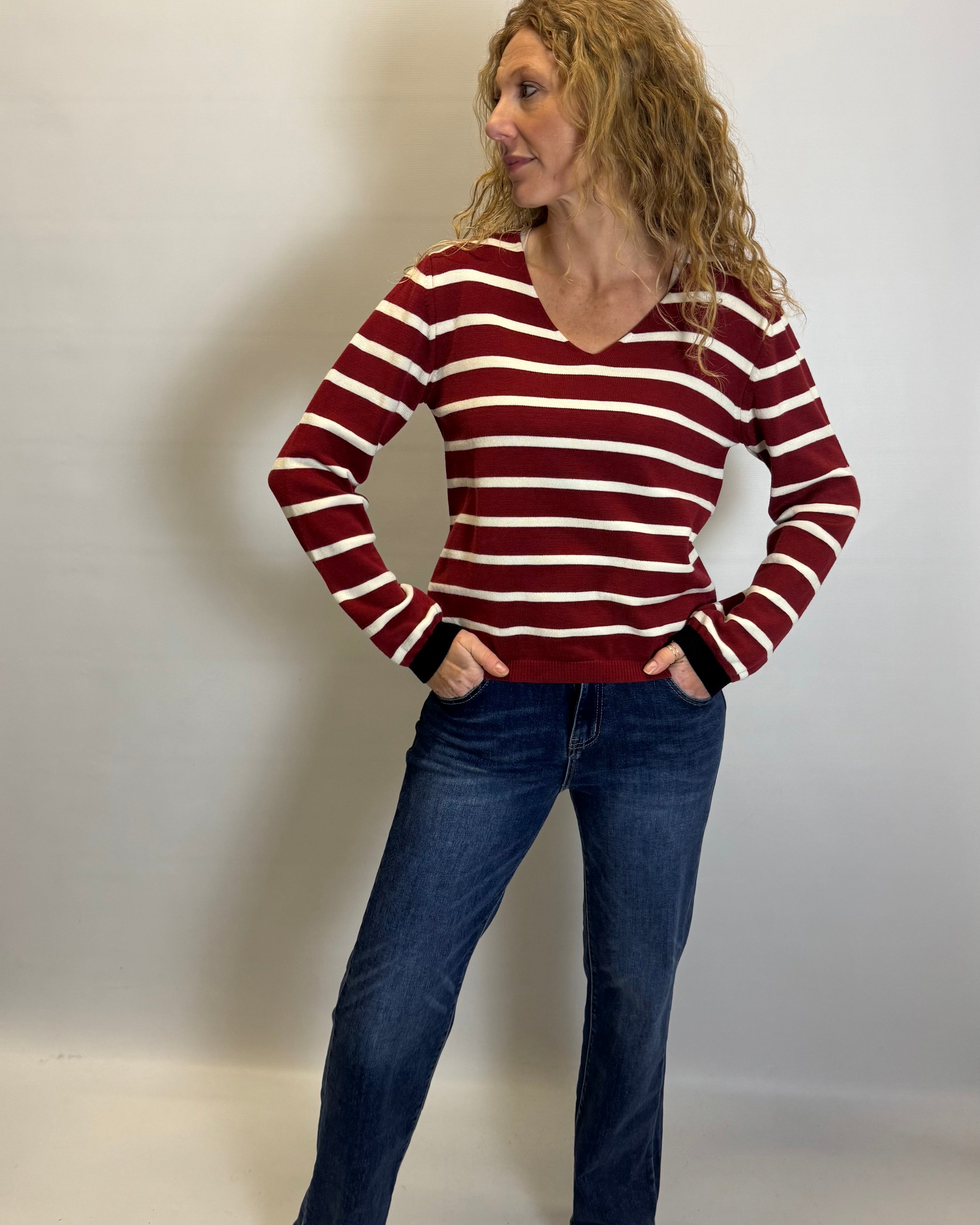 Woman wearing a red and white striped sweater and blue jeans against a plain background
