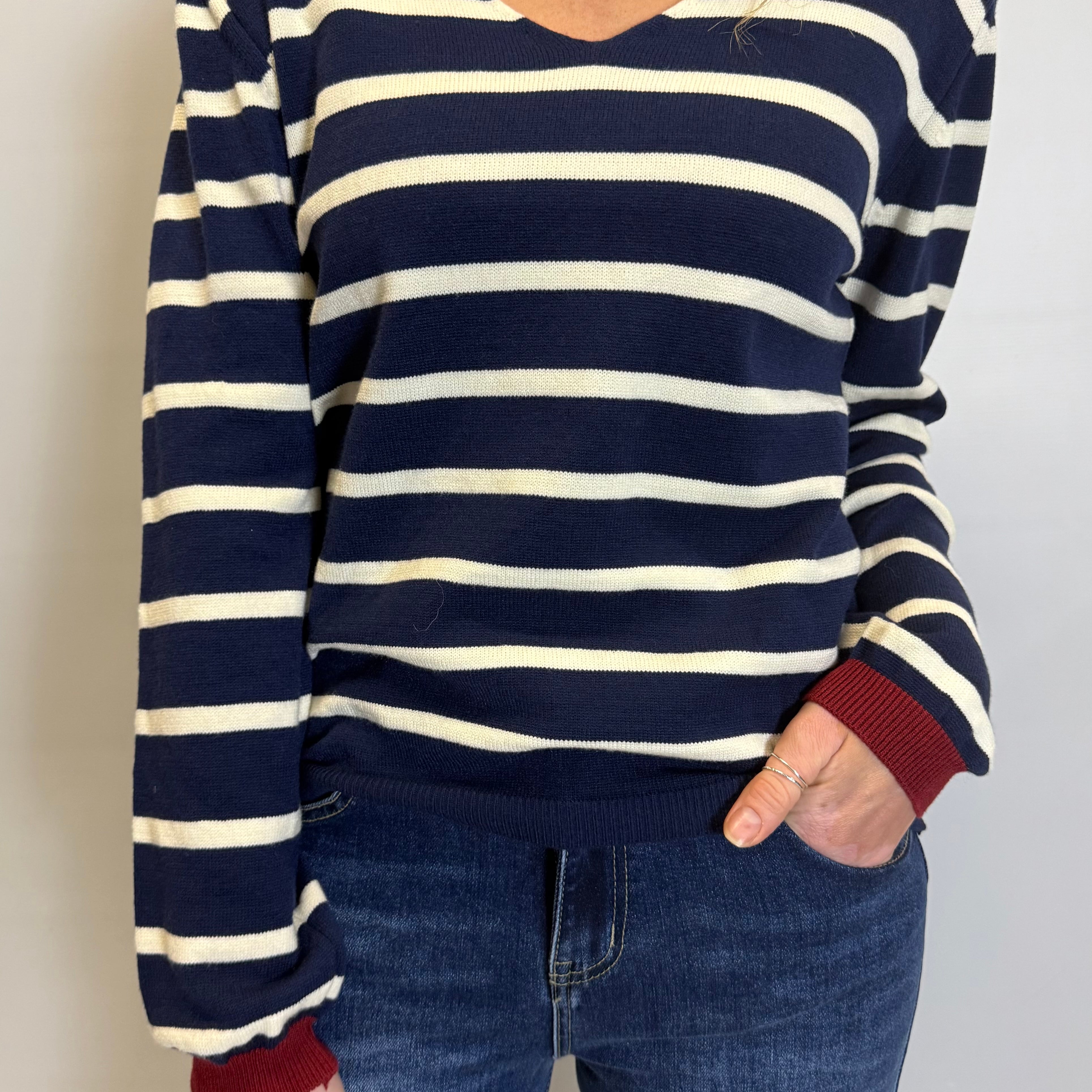 Person wearing a navy and white striped sweater with red cuffs and hem, paired with blue jeans.