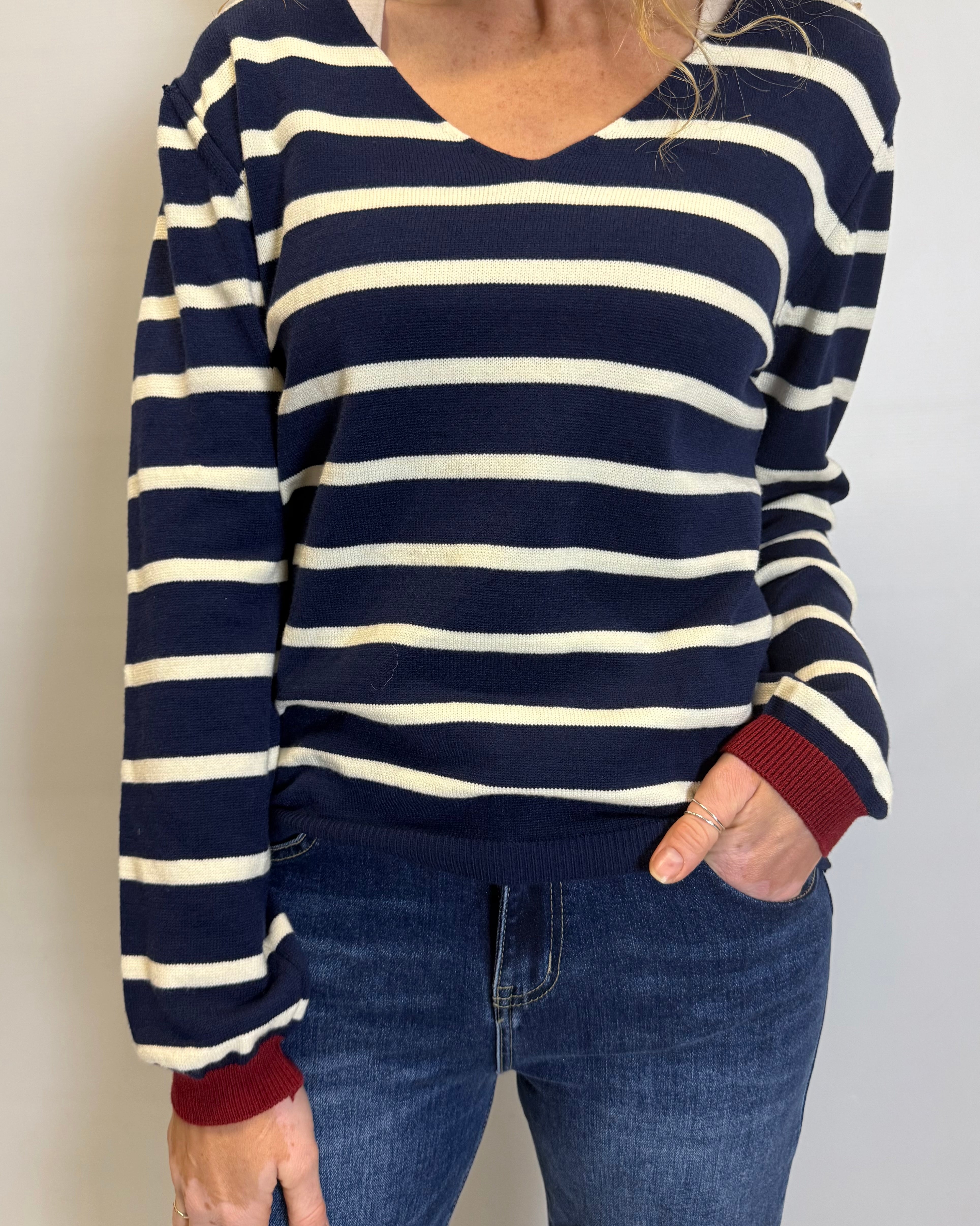 Person wearing a navy and white striped sweater with red cuffs and hem, paired with blue jeans.