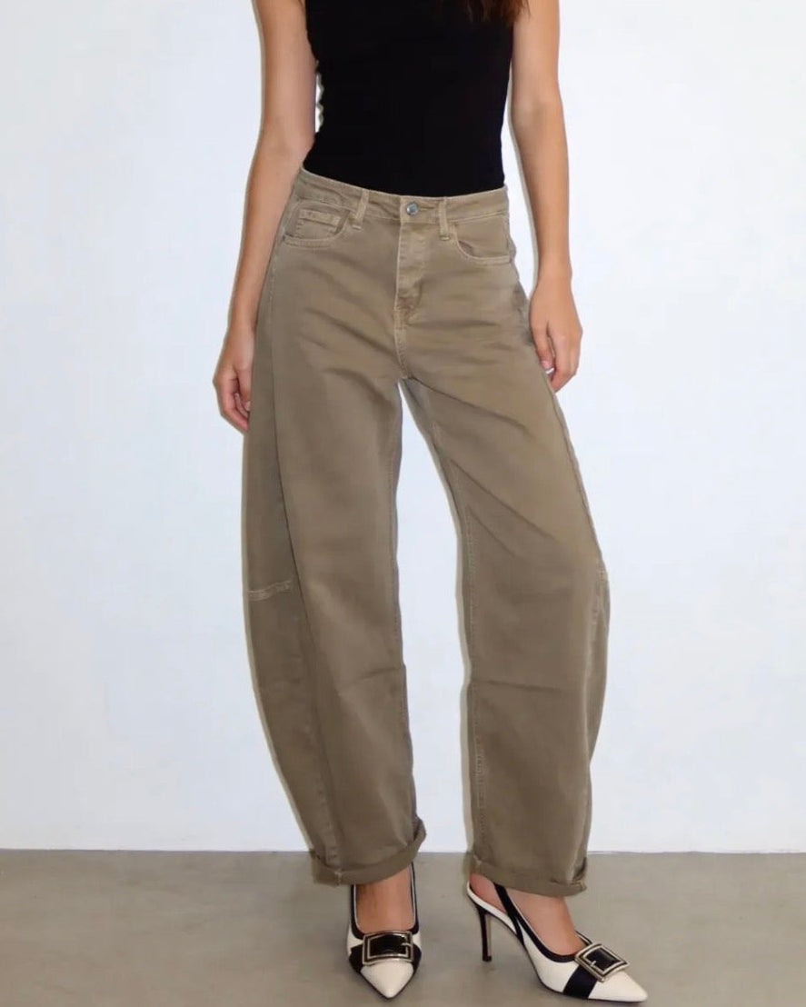 A model wearing a pair of wide-leg, cuffed khaki cargo pants, styled with a black tank top and black-and-white pointed-toe heels against a plain white wall.