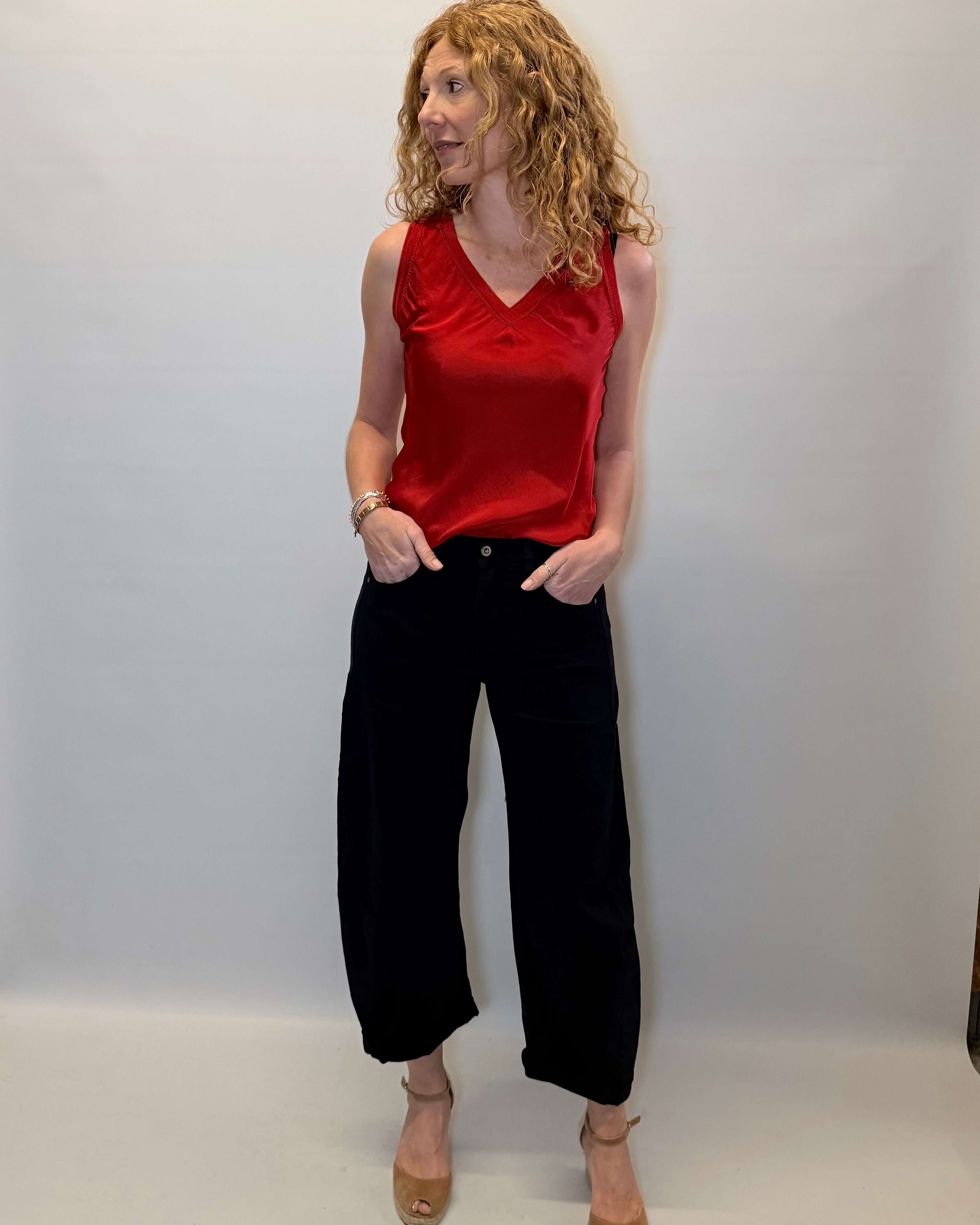 Woman wearing a red sleeveless top and black pants against a plain background