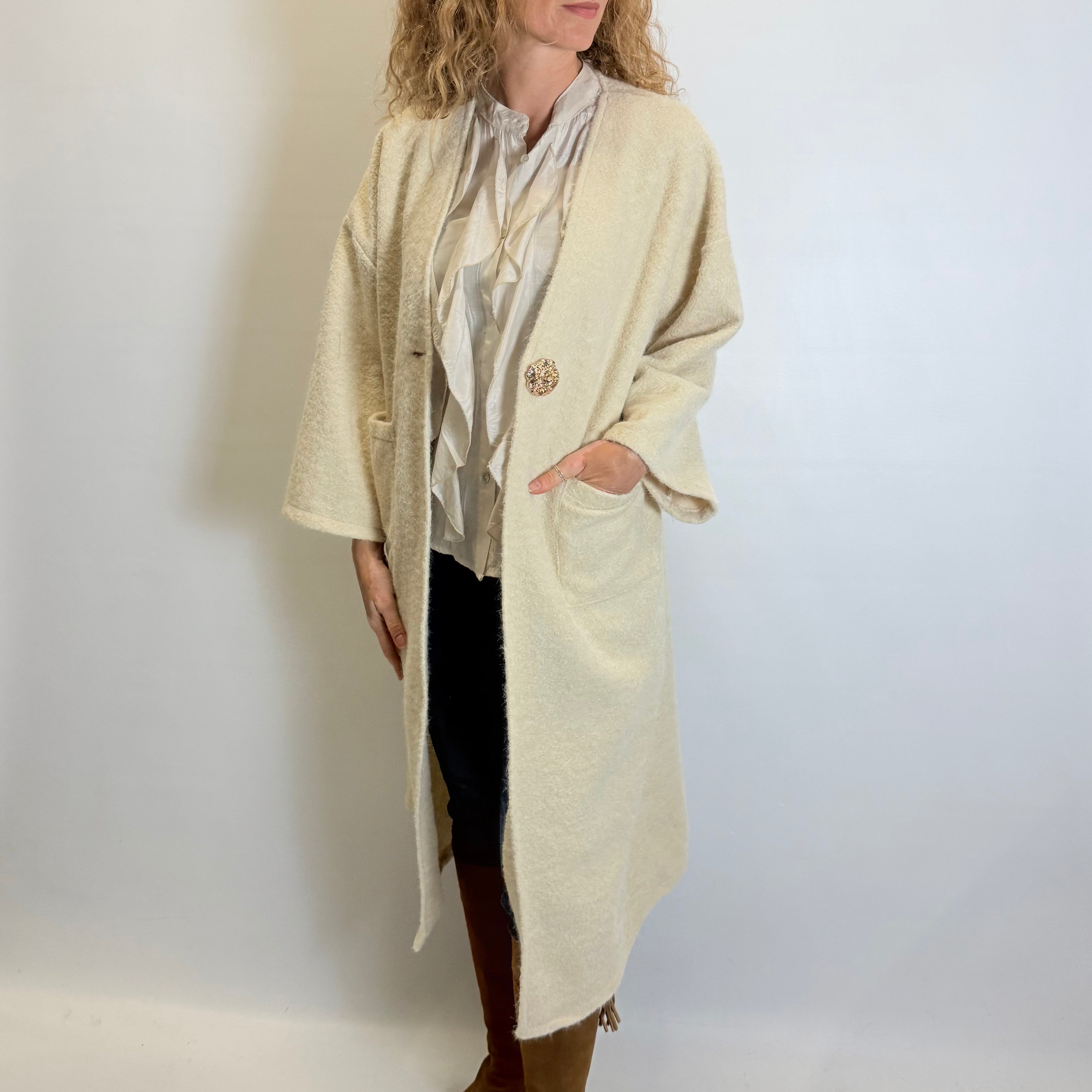 Woman wearing a long beige coat over a patterned top with a plain background