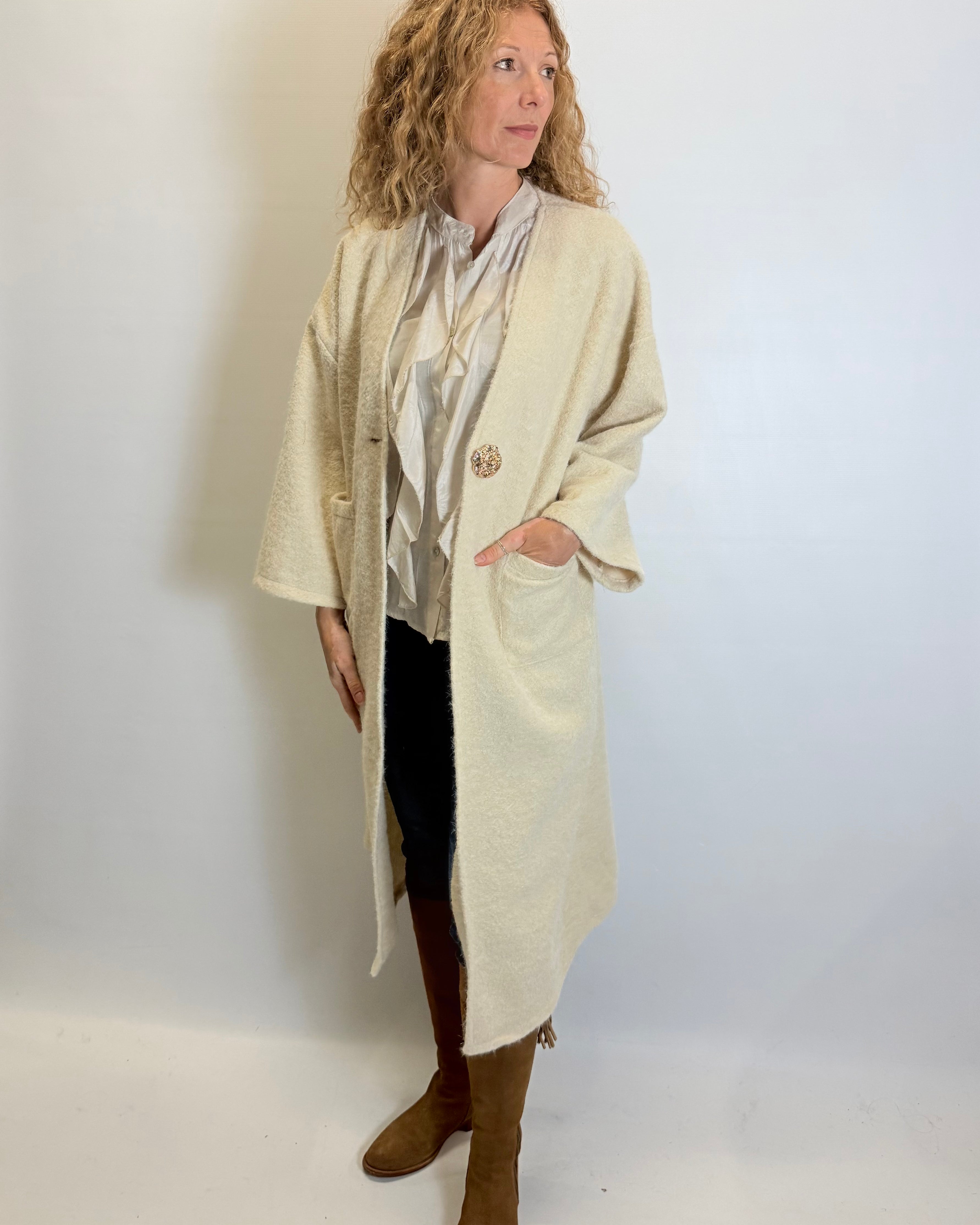 Woman wearing a long beige coat over a patterned top with a plain background