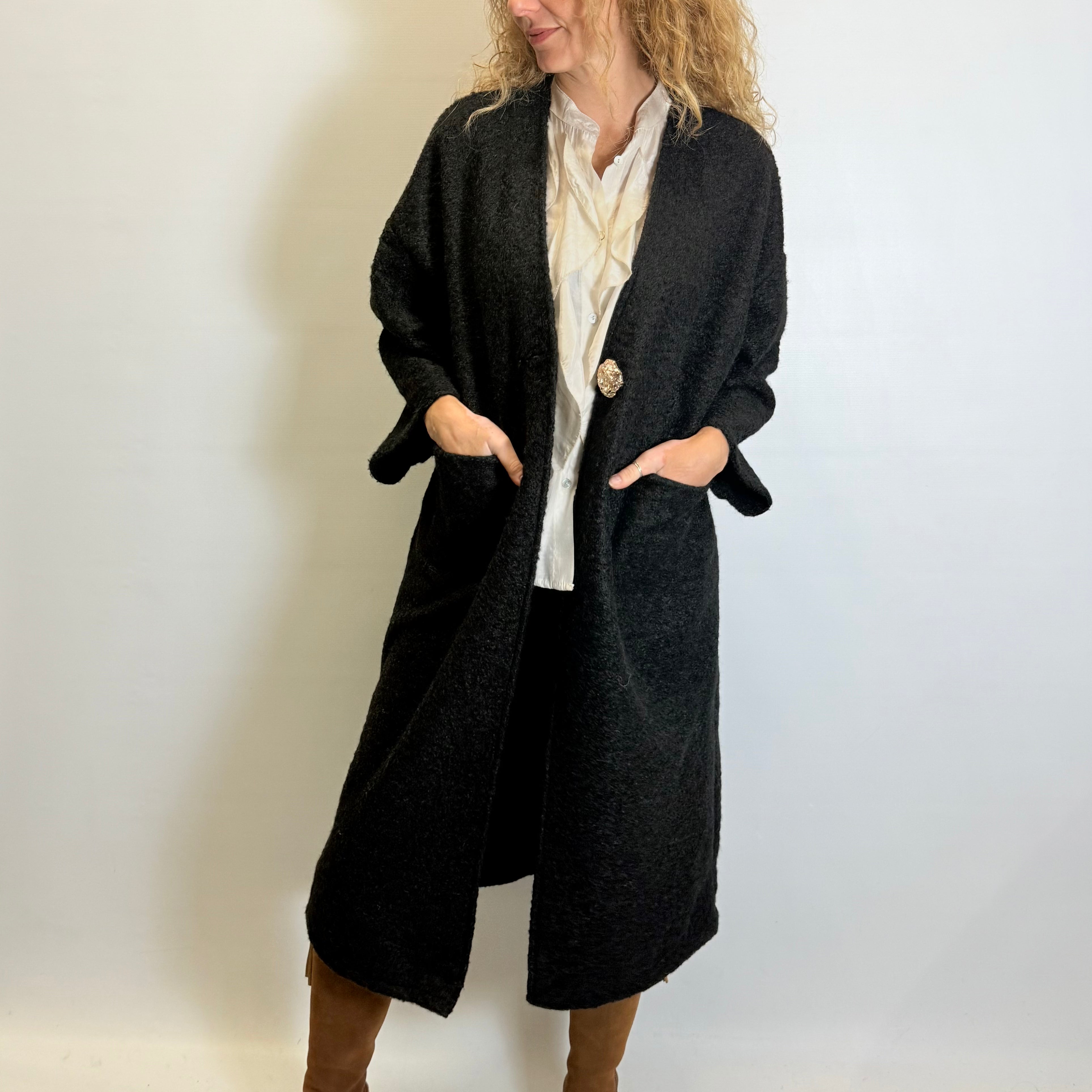 Woman wearing a long black coat over a white shirt on a plain background