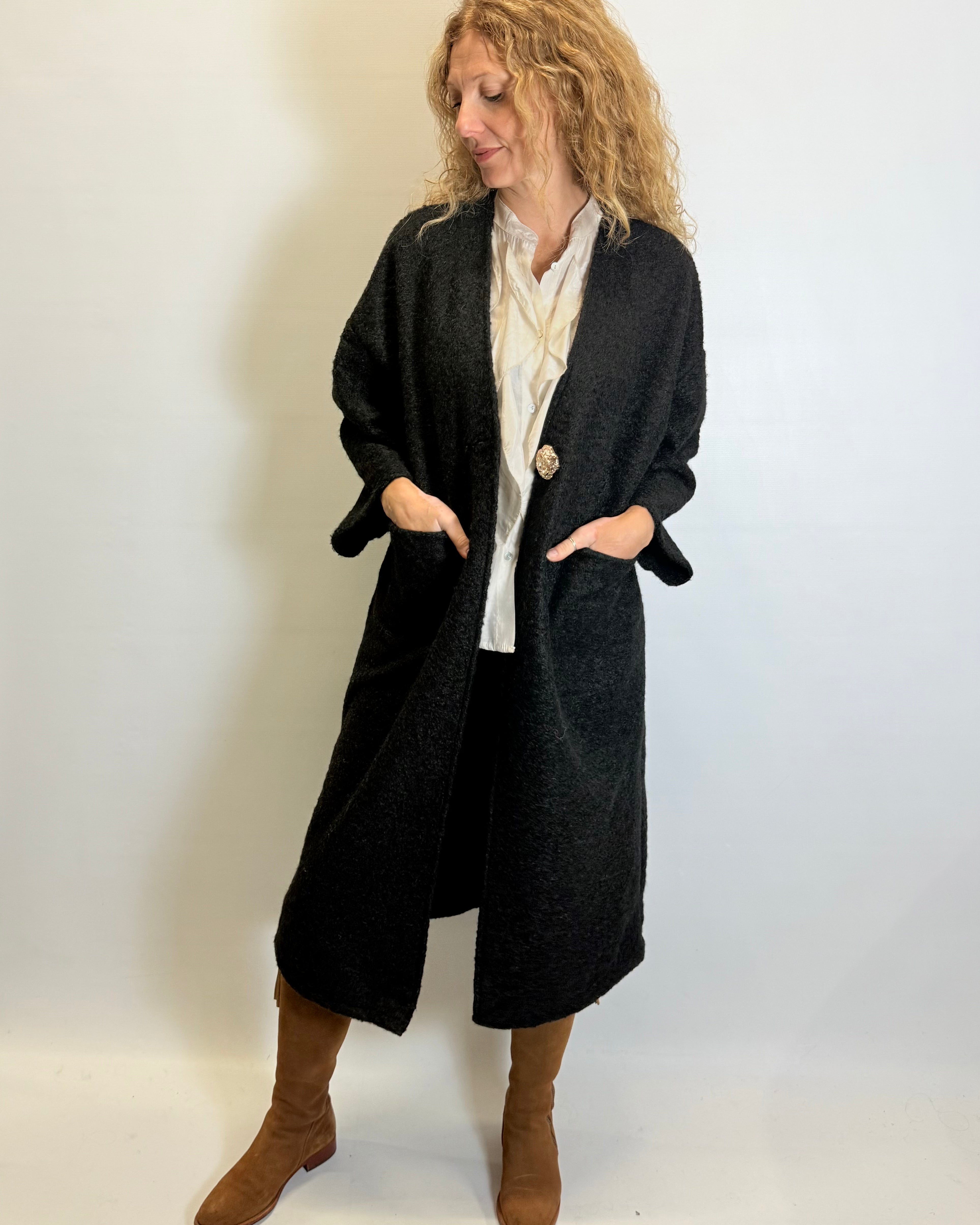 Woman wearing a long black coat over a white shirt on a plain background