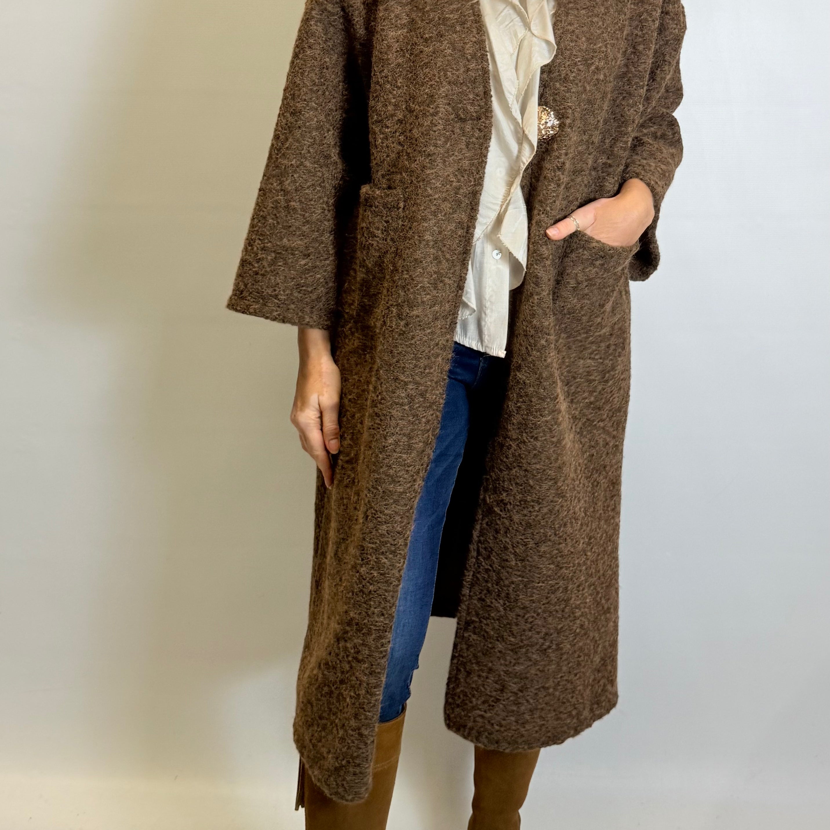 Person wearing a long brown coat with a plain background