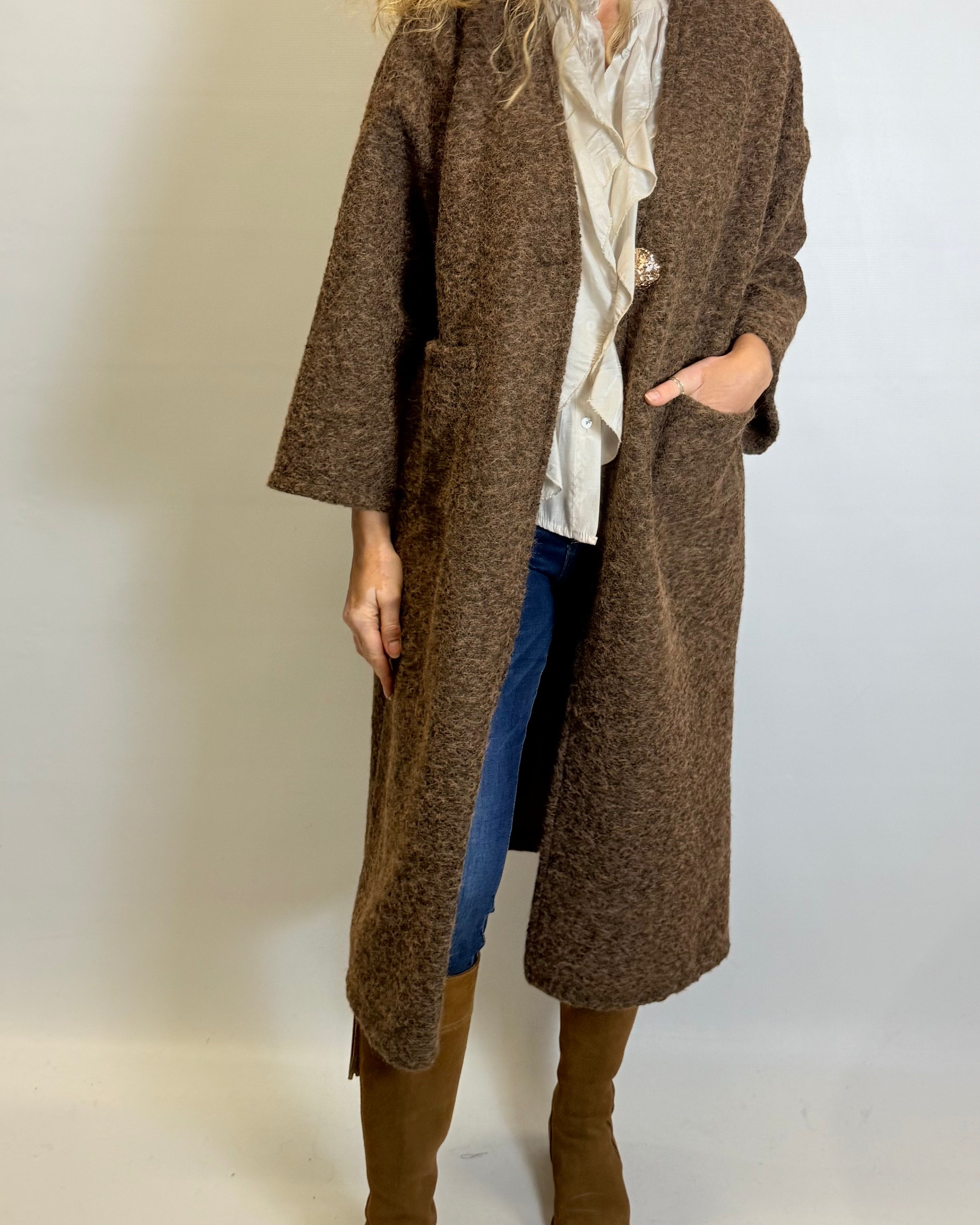 Person wearing a long brown coat with a plain background