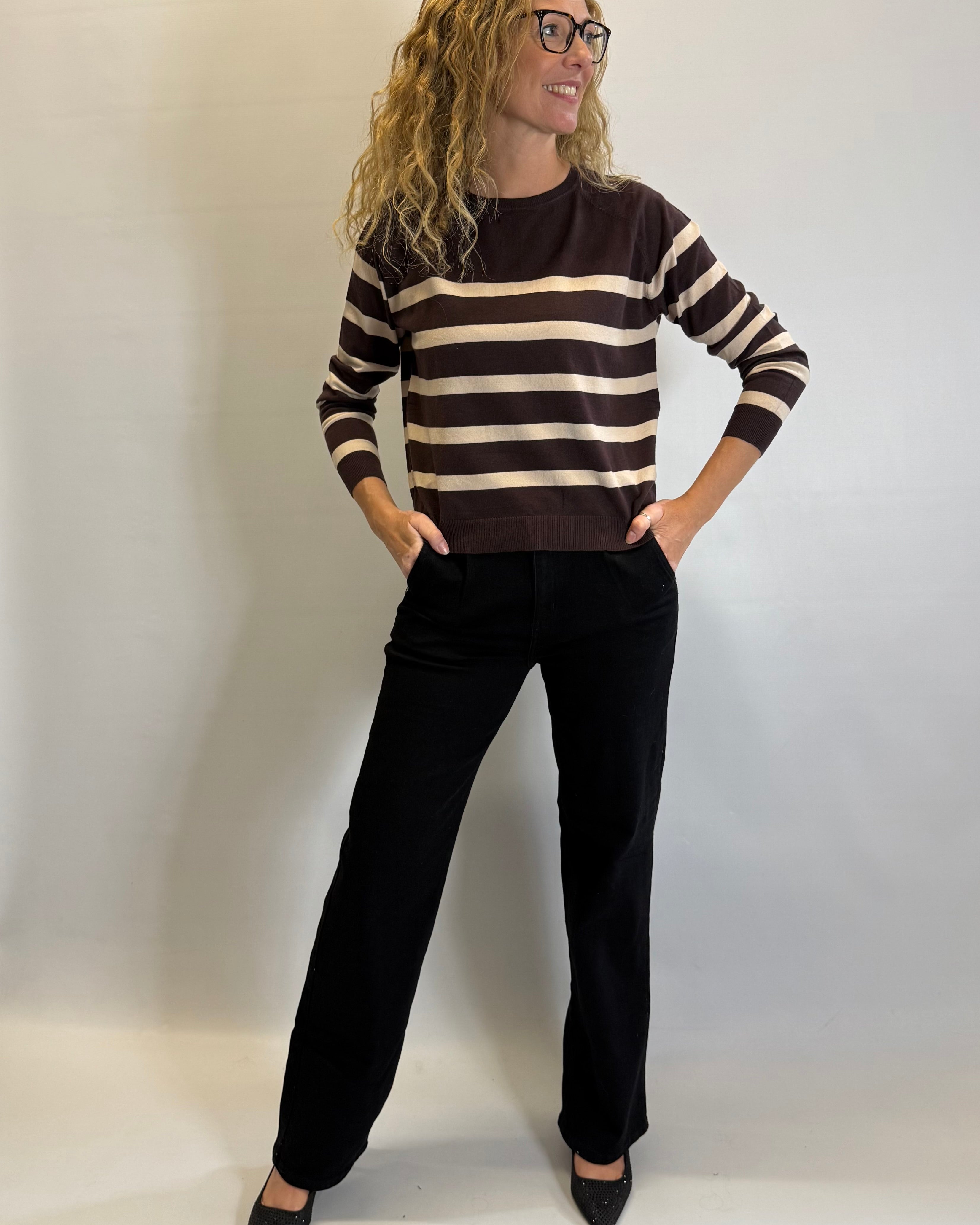 Woman wearing a brown and white striped sweater with black pants against a plain background
