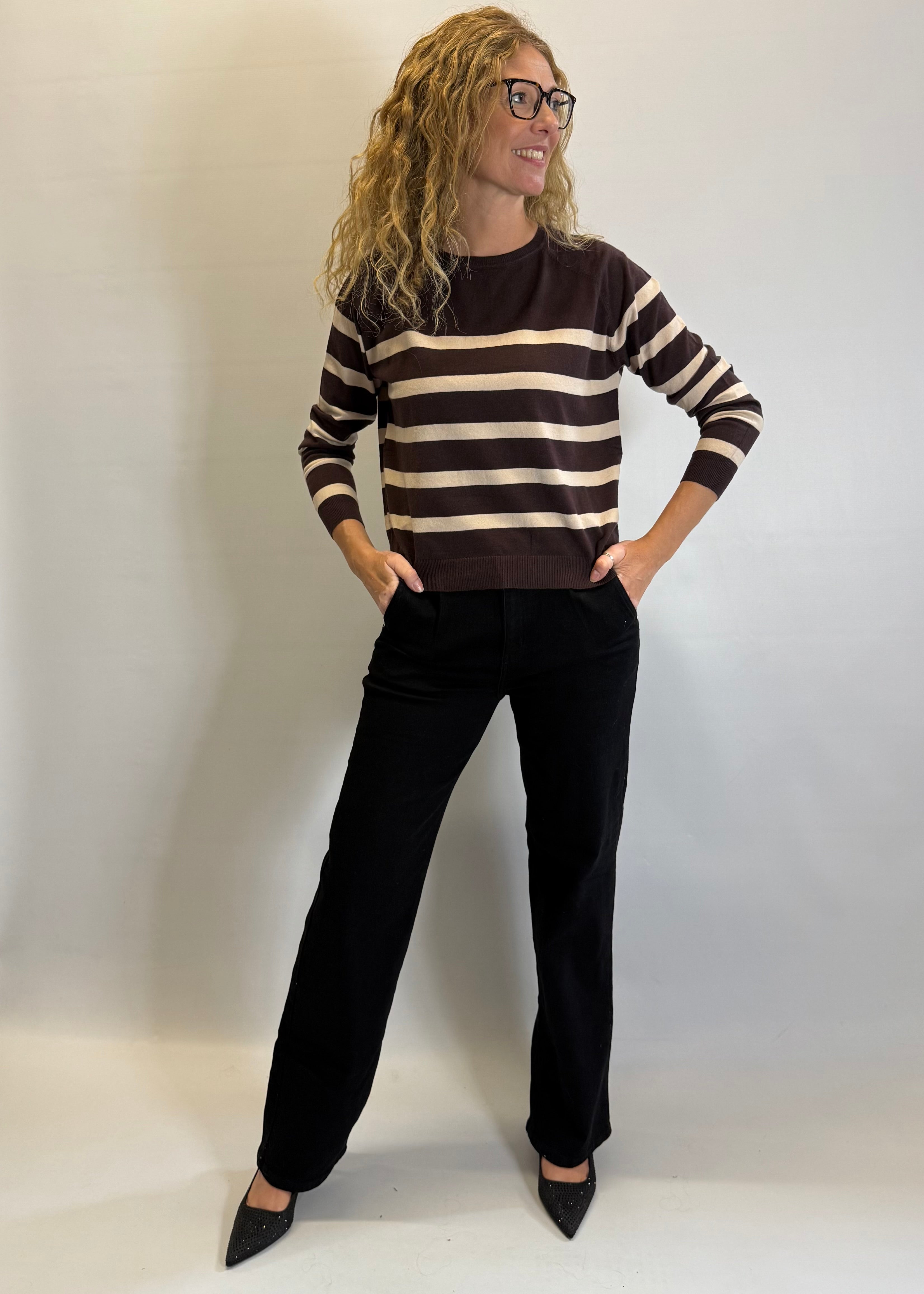 Woman wearing a brown and white striped sweater with black pants against a plain background