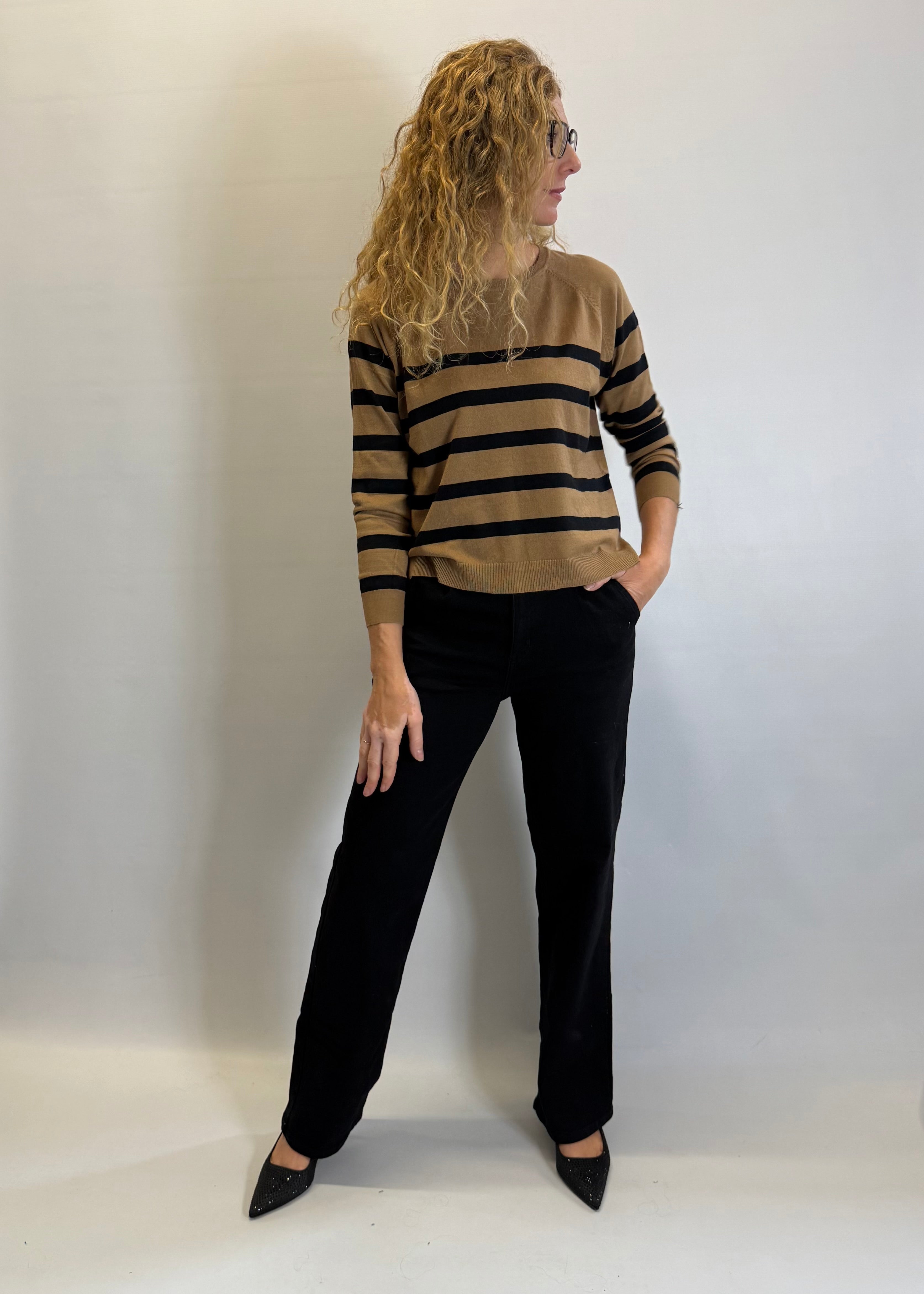 Woman wearing a striped sweater and black pants against a white background