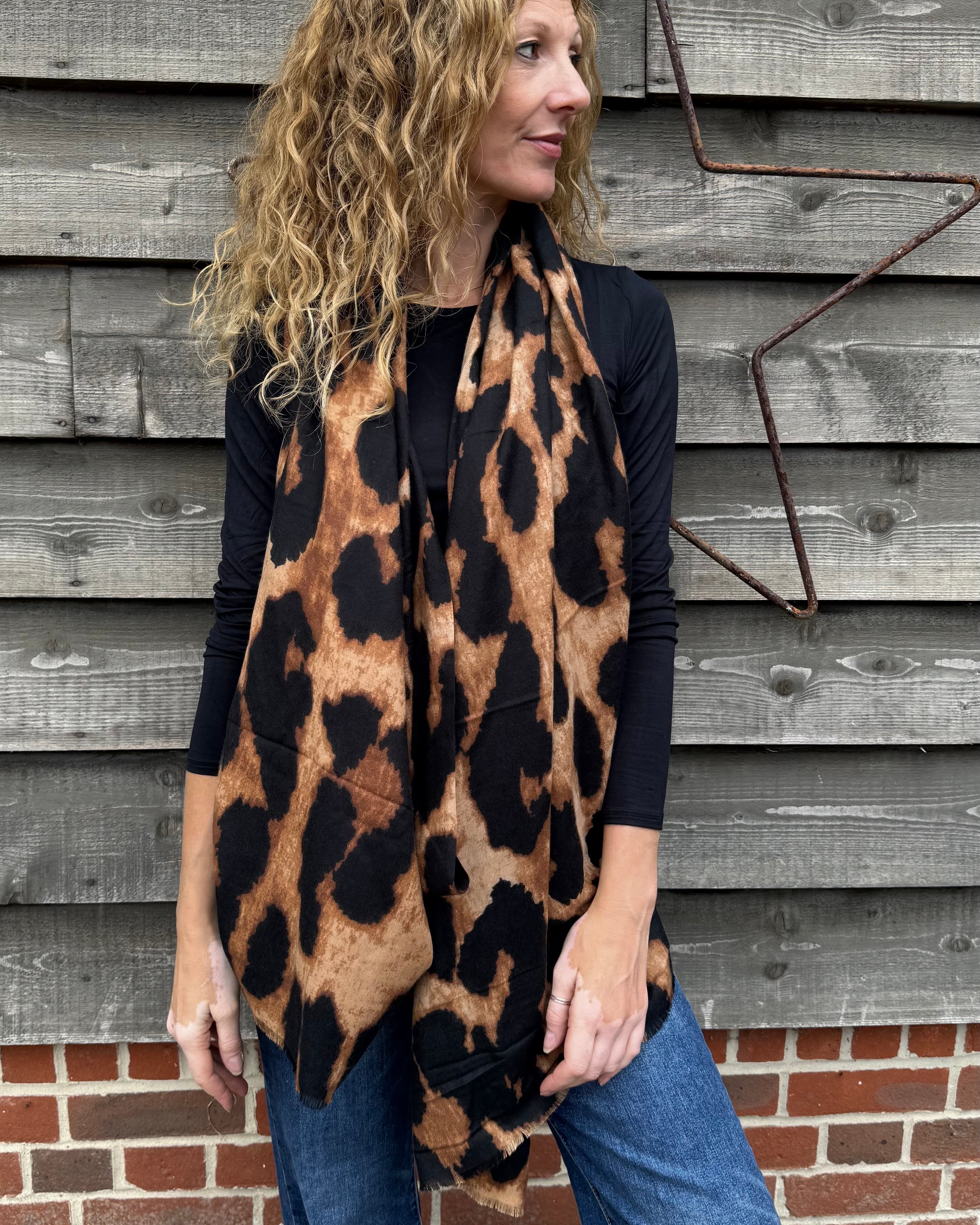 Woman wearing a leopard print poncho in front of a wooden wall.