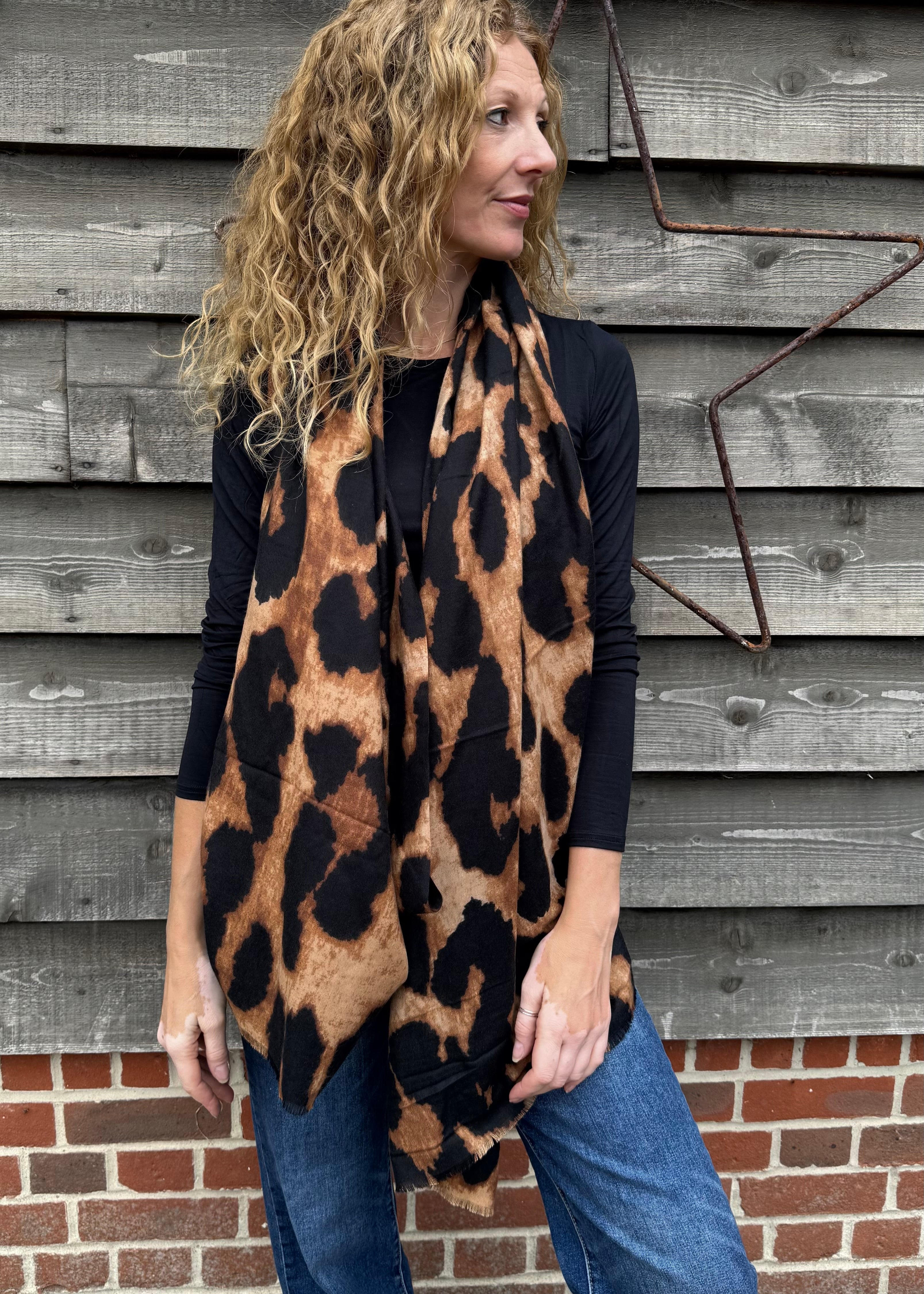 Woman wearing a leopard print poncho in front of a wooden wall.