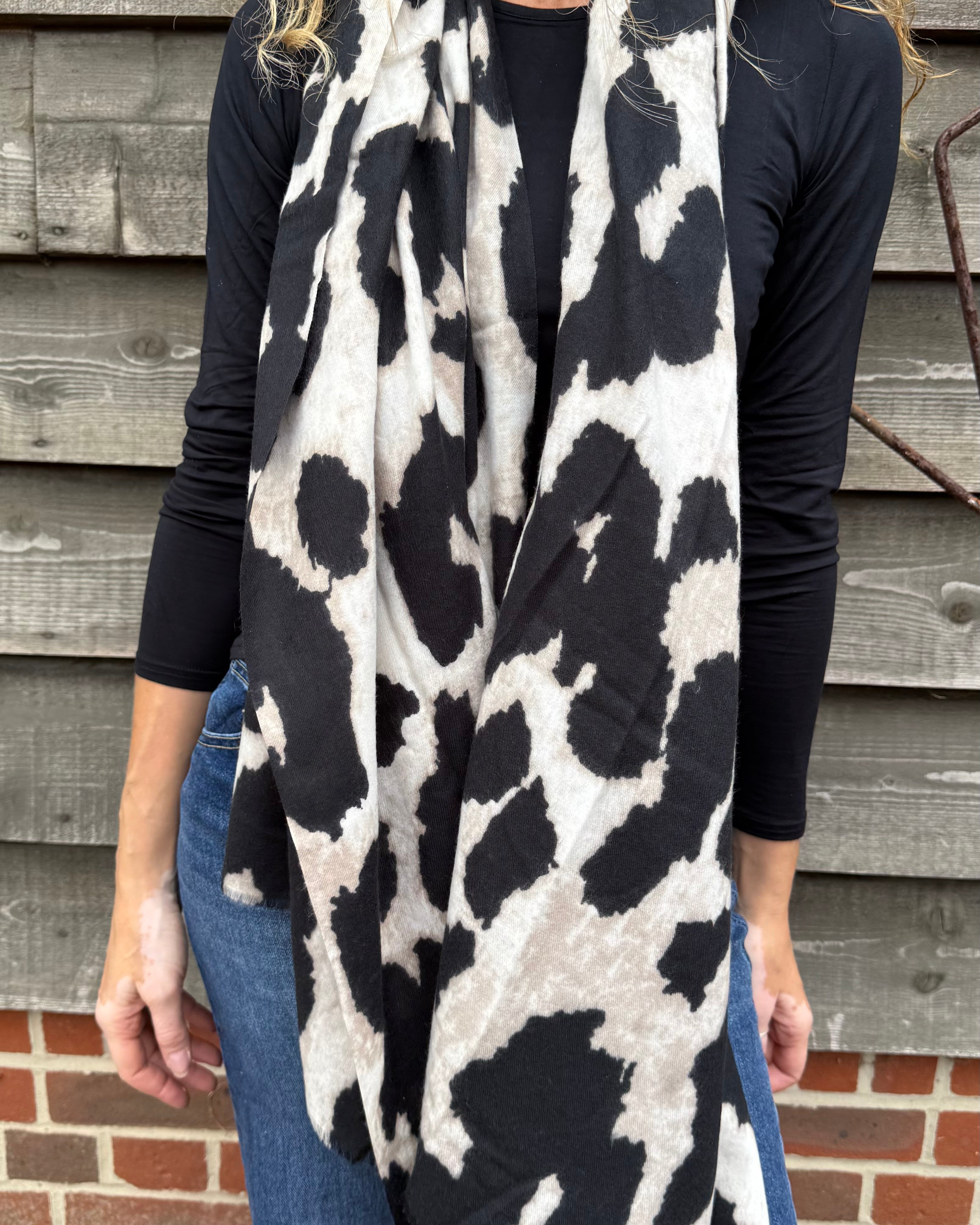 Person wearing a black and white patterned scarf in front of a wooden wall.