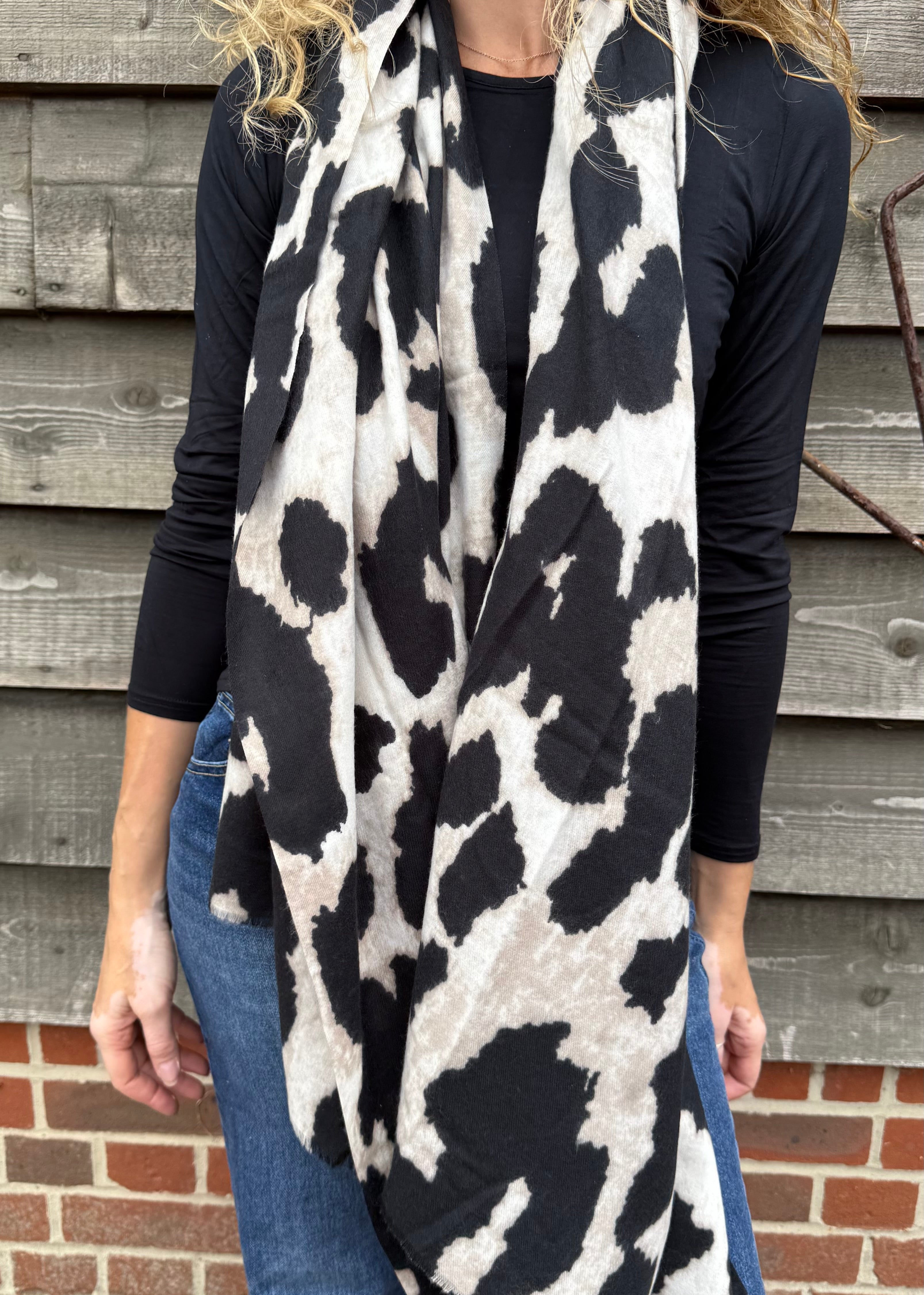 Person wearing a black and white patterned scarf in front of a wooden wall.