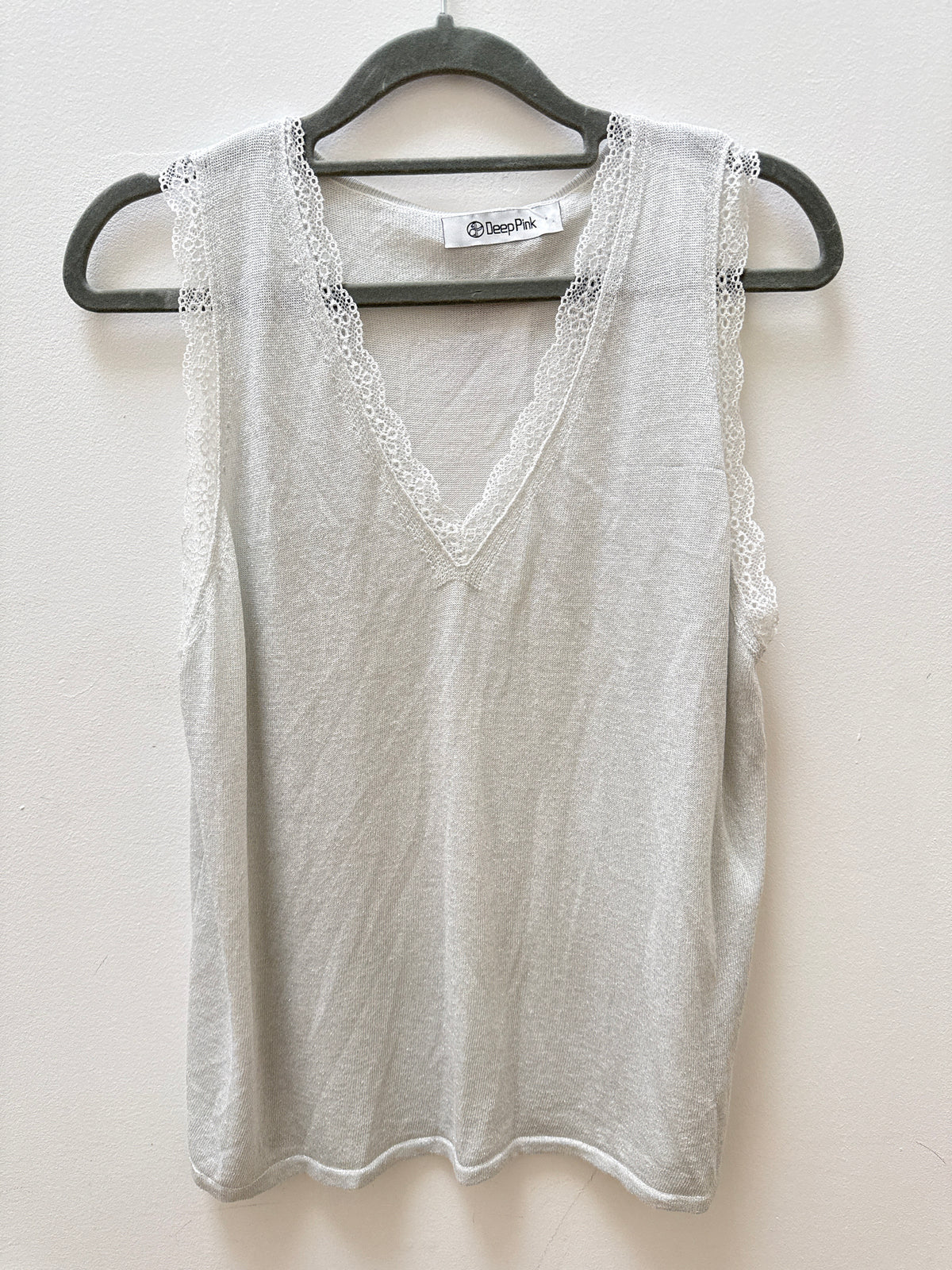 A light gray sleeveless V-neck top with delicate lace trim along the armholes and neckline, hanging on a black hanger against a plain off-white wall.