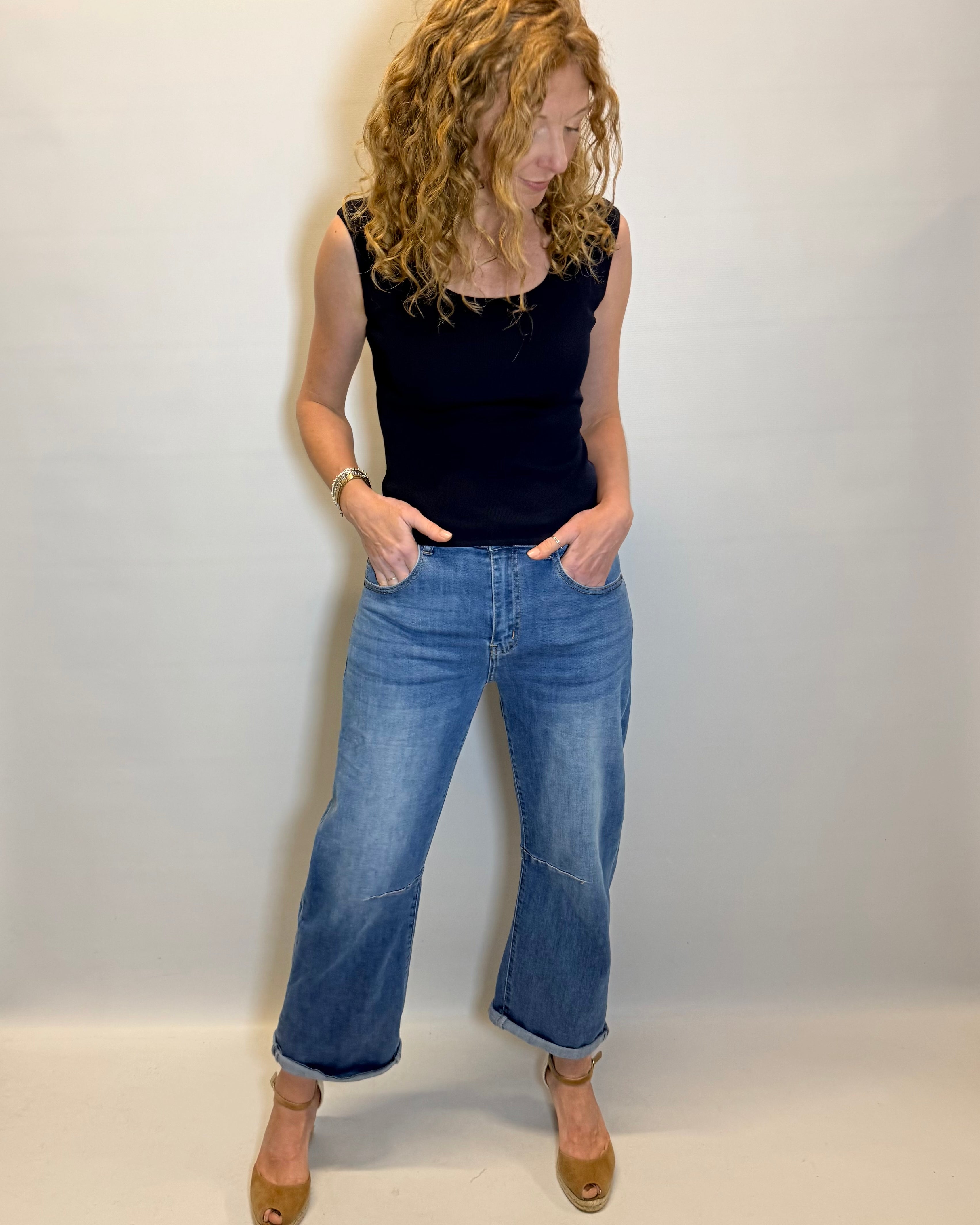 Woman wearing a black top and blue jeans against a white background